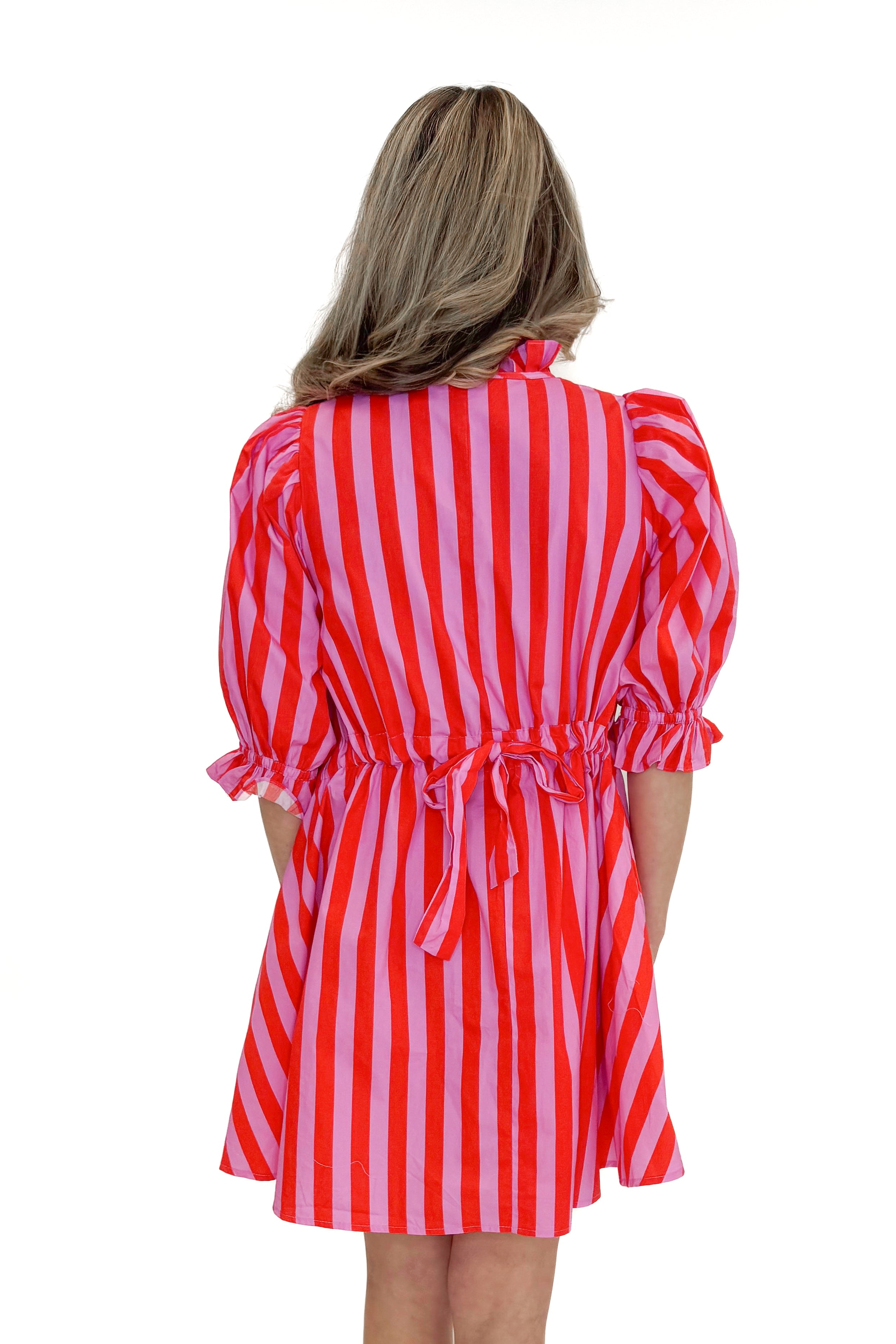 Back view of woman wearing Pink & Red Striped Tie Back Dress by Entro with sandals against white studio background.