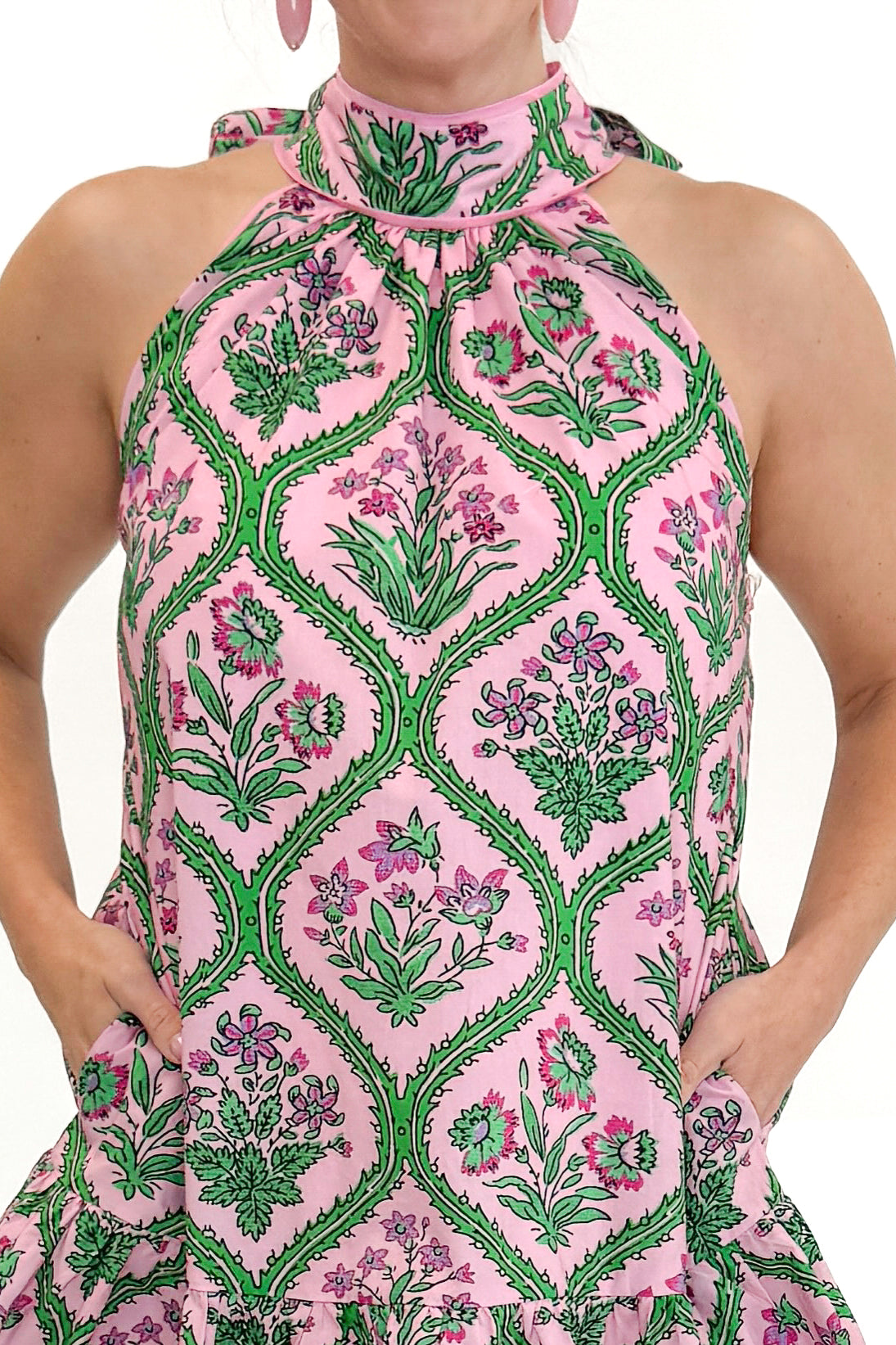 Front detail view of woman wearing Pink & Green Floral Halter Neck Dress by Entro against white studio background.