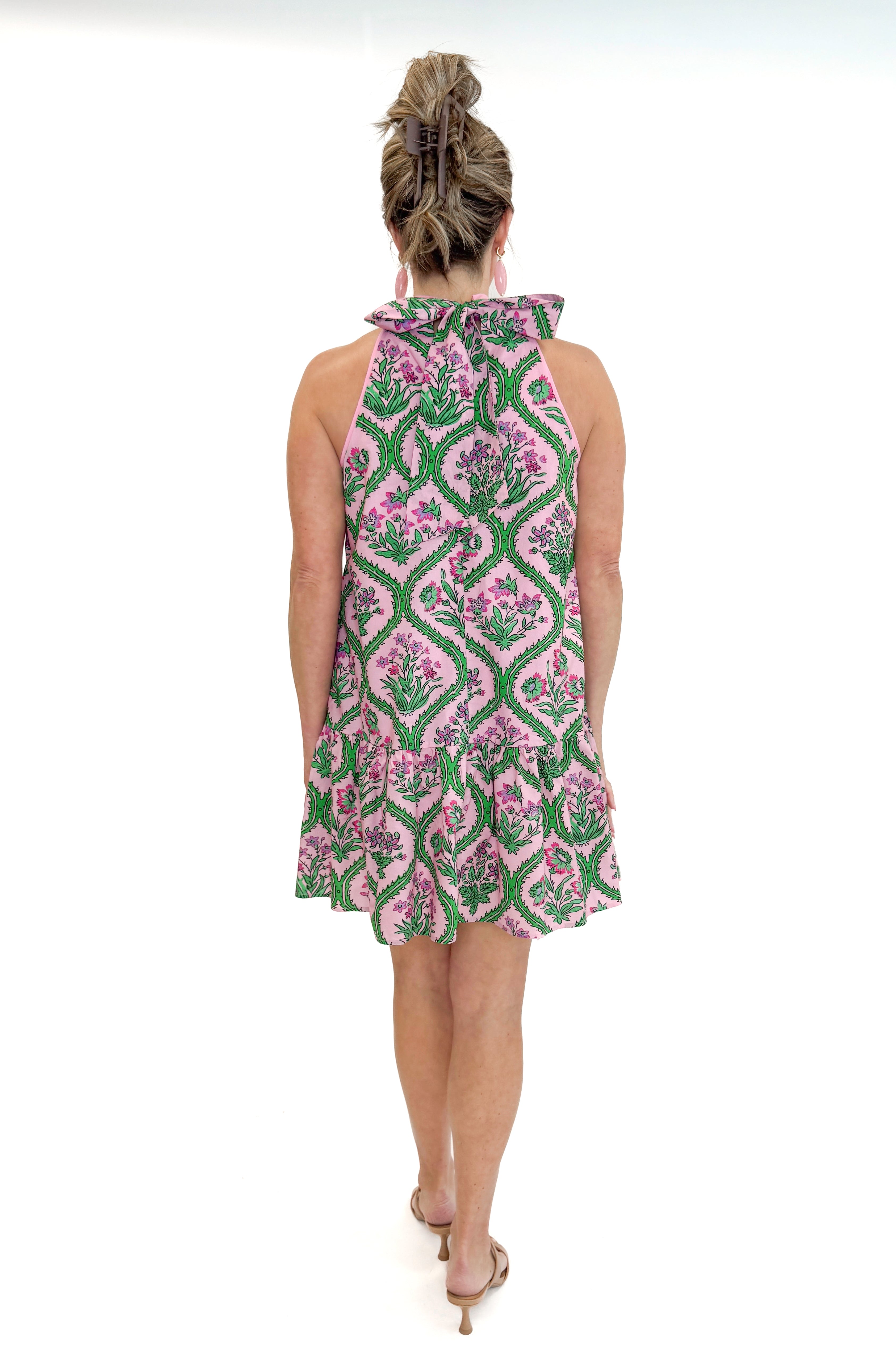 Back view of woman wearing Pink & Green Floral Halter Neck Dress by Entro against white studio background.