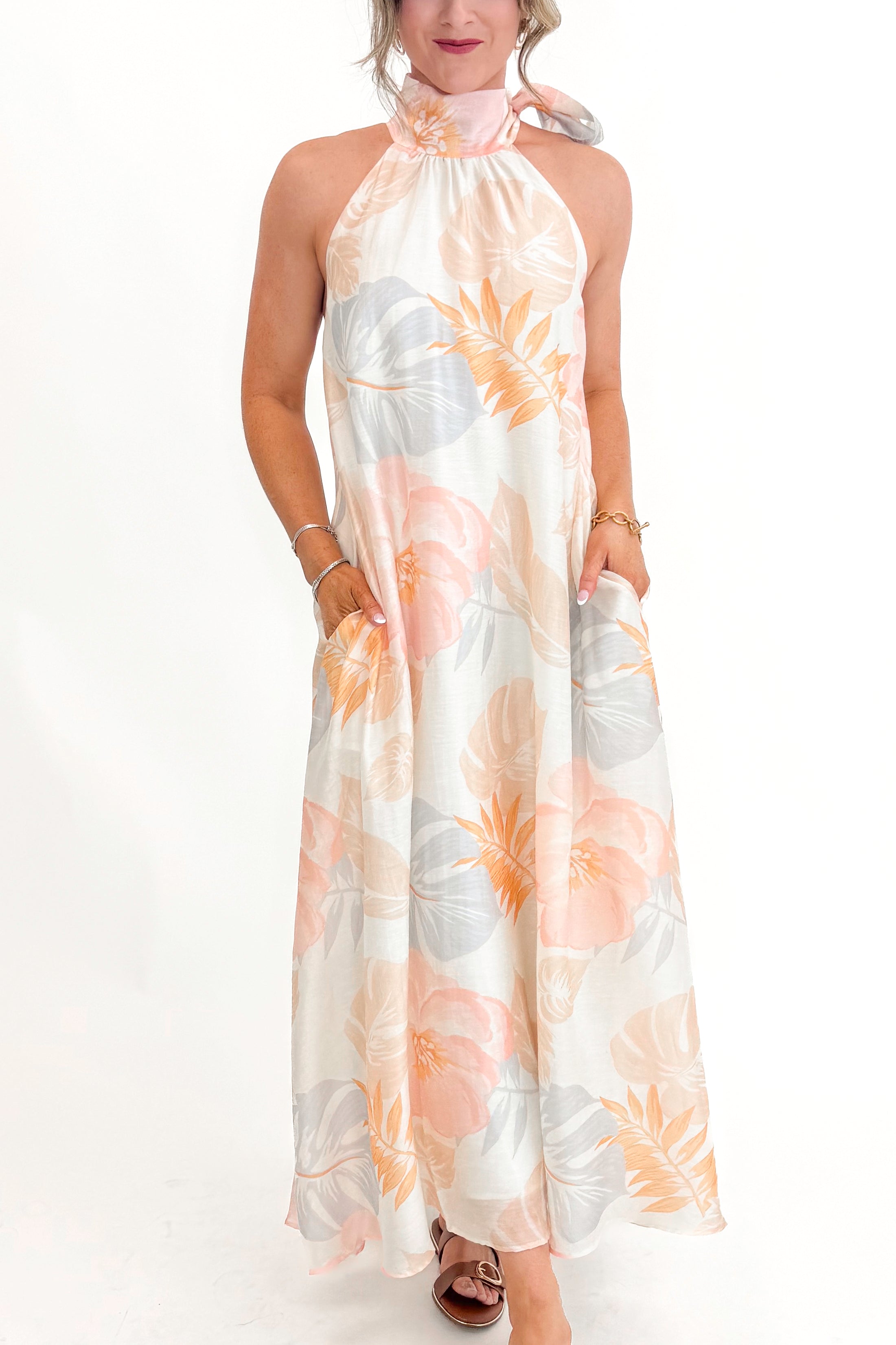 Front view of woman wearing Multi Tropical Printed Tie Neck Maxi Dress by Entro with sandals against white studio background.