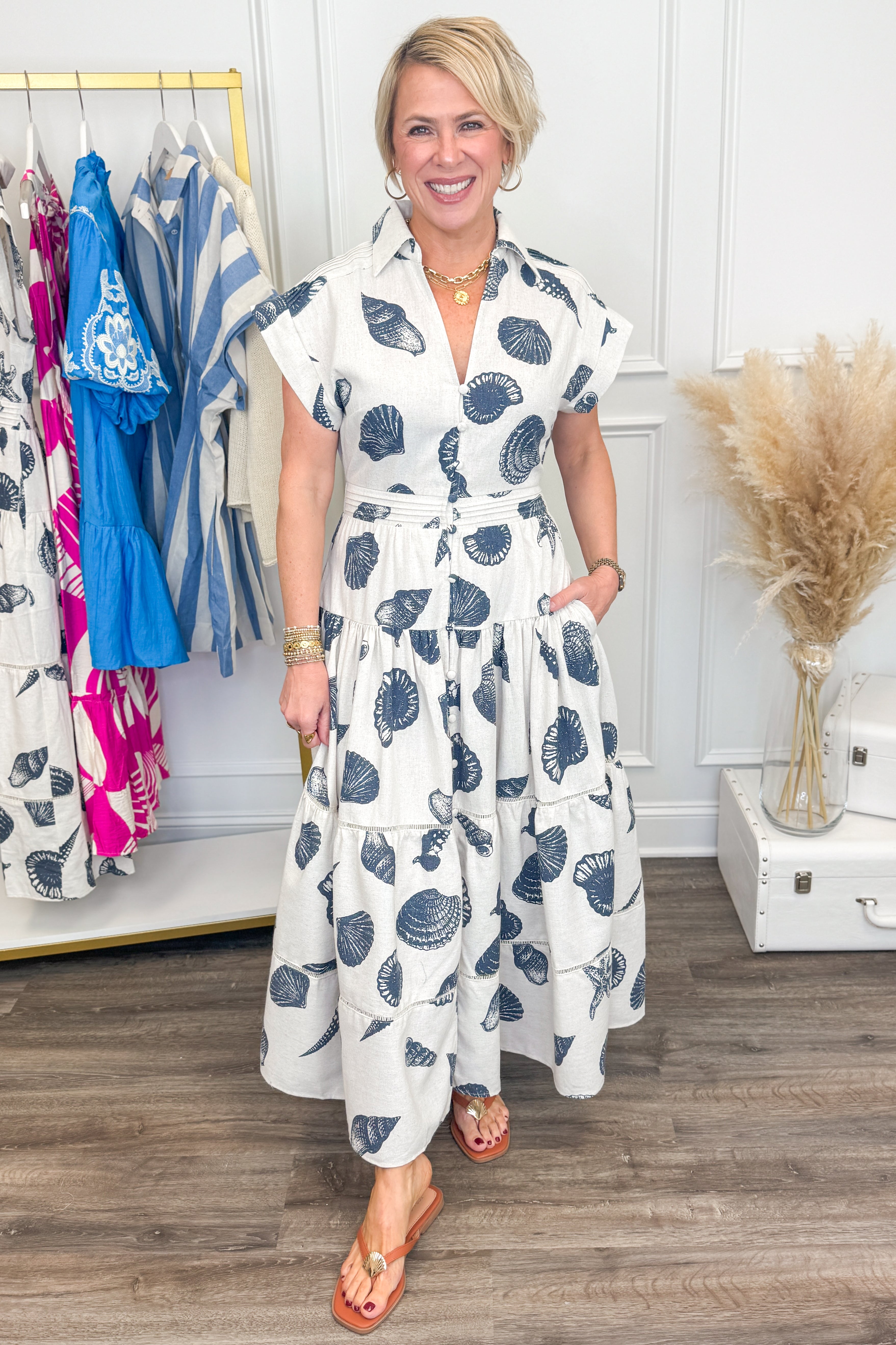 Woman wearing a white dress with blue patterns in a room with clothing racks and decor.