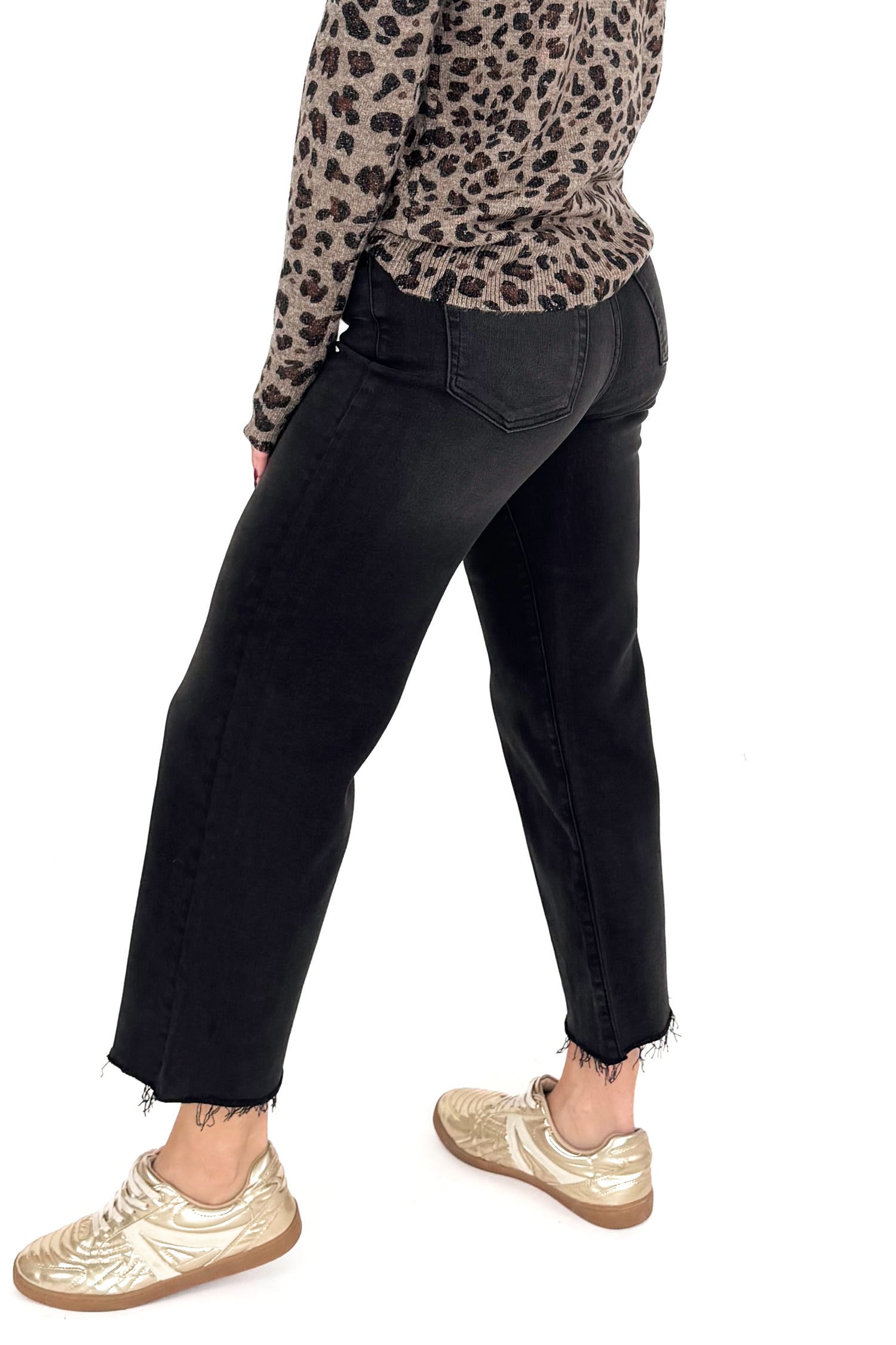 Side view of woman wearing washed black jeans and print top against white studio background.