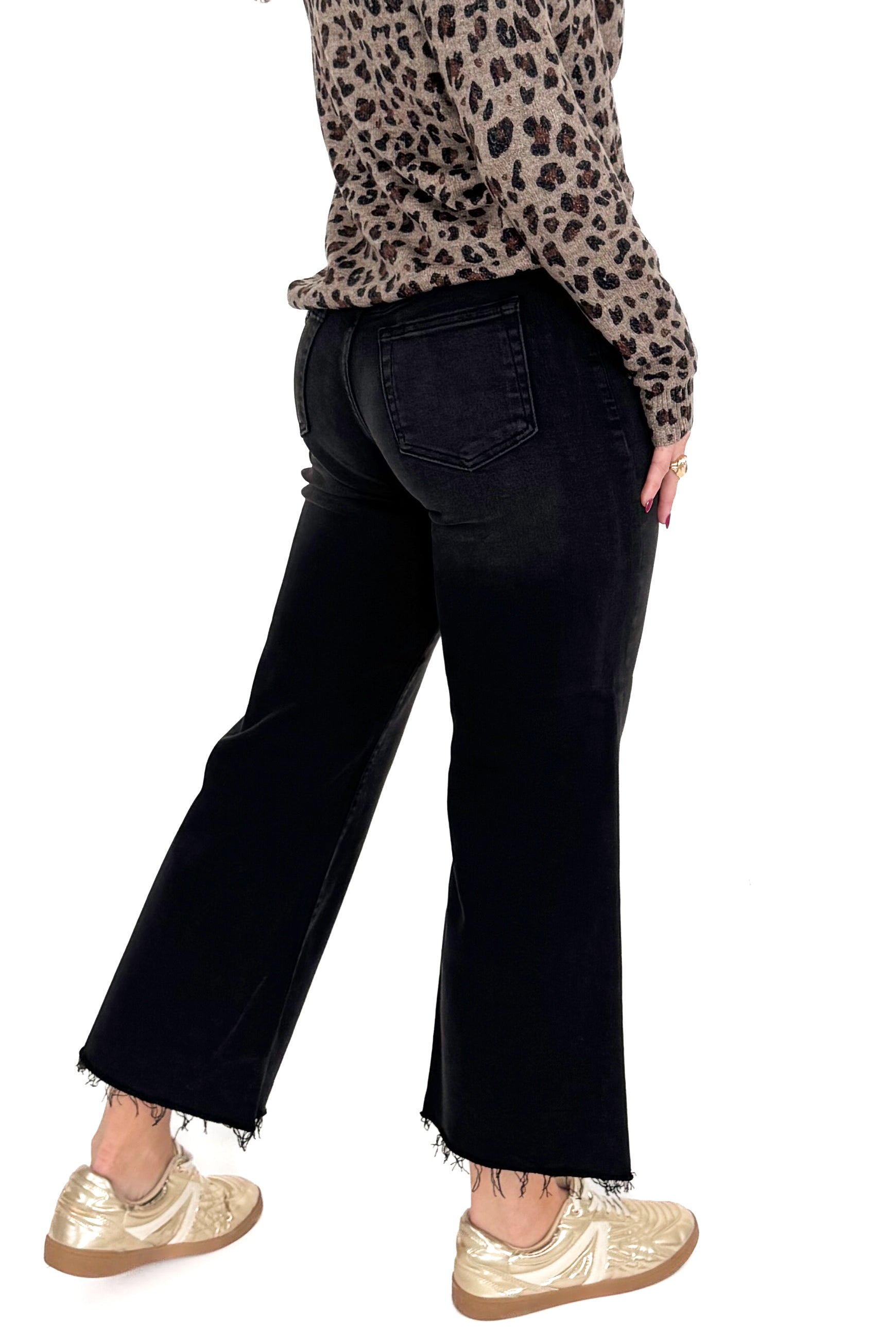 Side view of woman wearing washed black jeans and print top against white studio background.