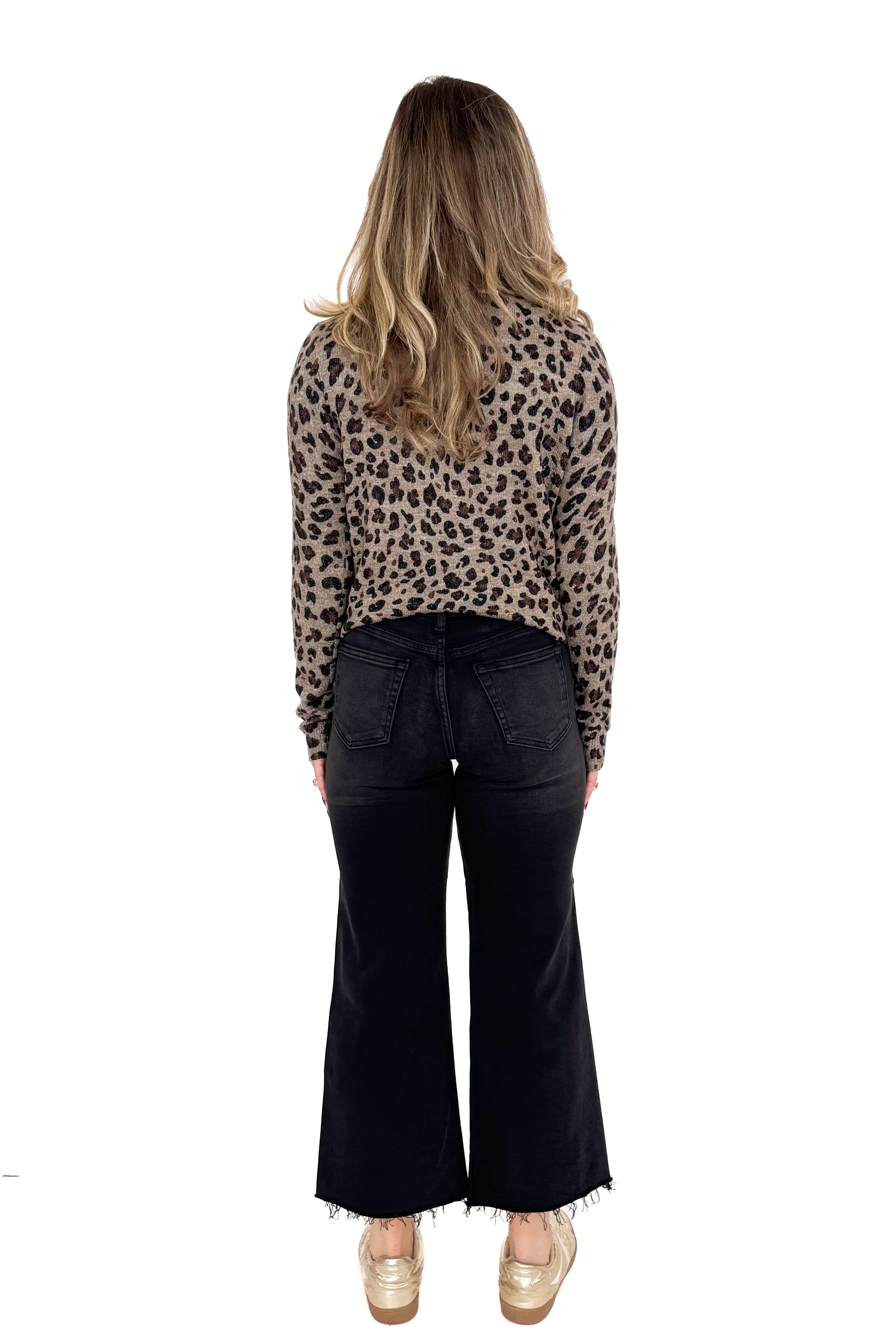 Back view of woman wearing washed black jeans and print top against white studio background.