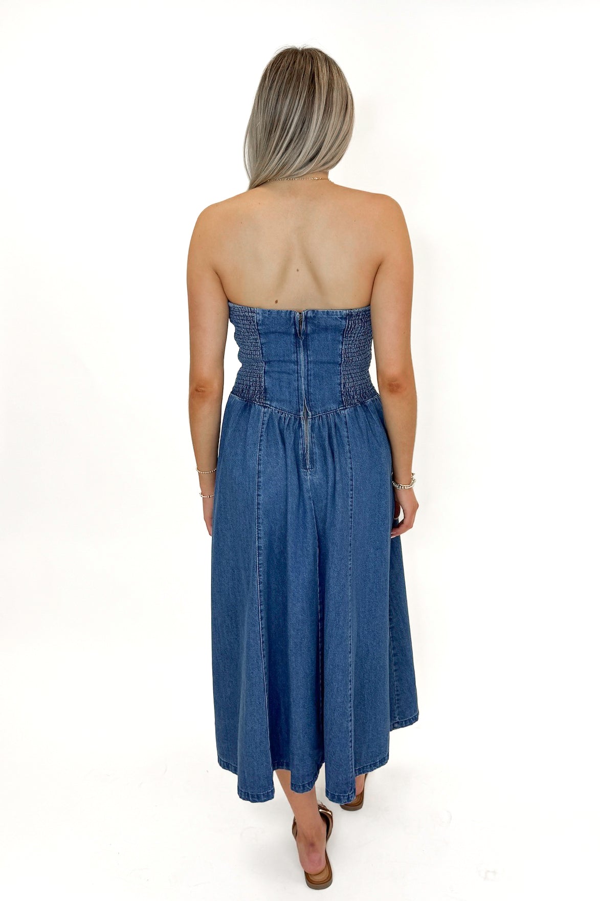 Back view of woman wearing Denim V-Waist Midi Dress with sandals against white studio background.