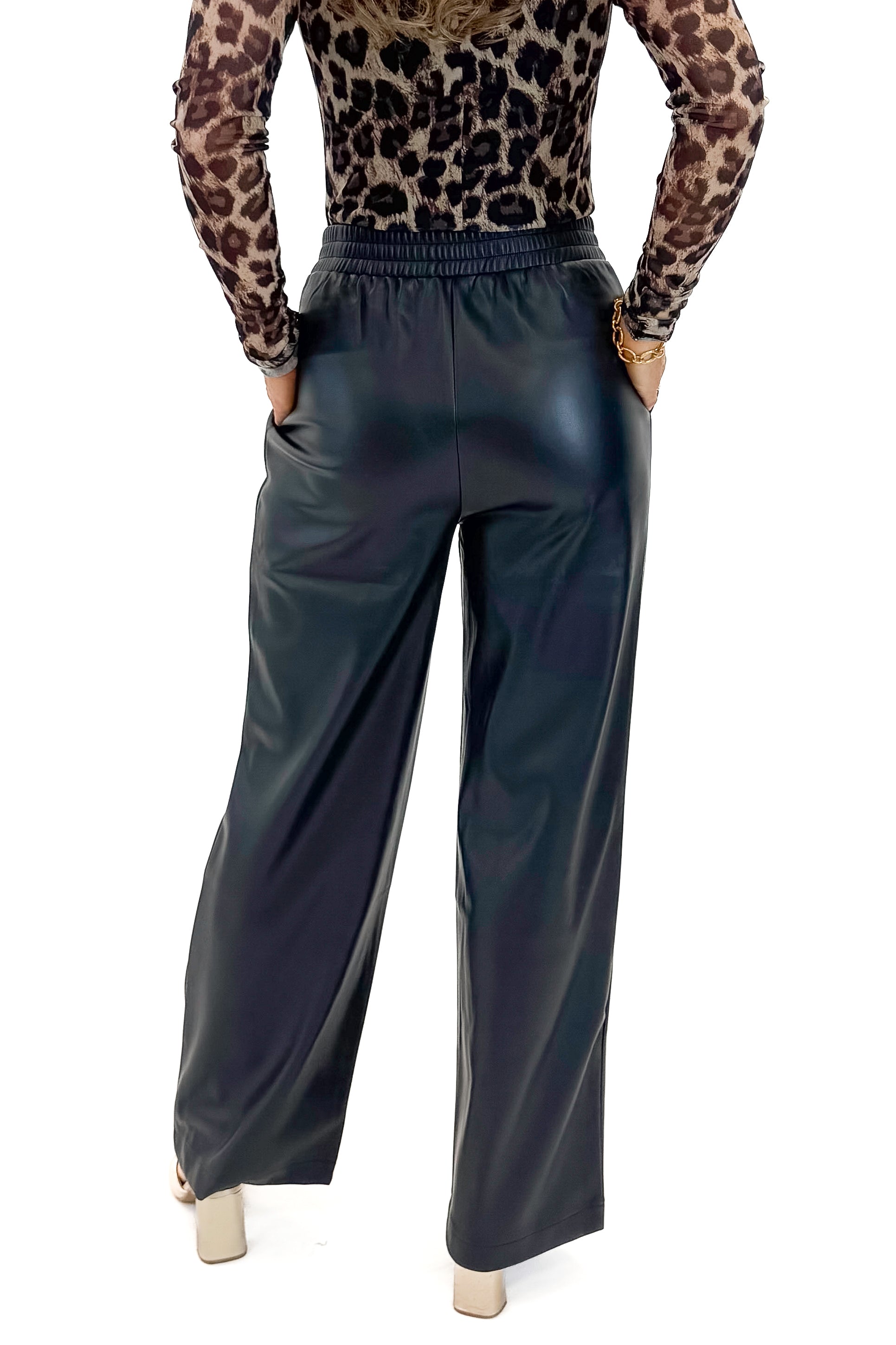 Back view of woman wearing Black Faux Leather Pants with leopard mesh top against white studio background.