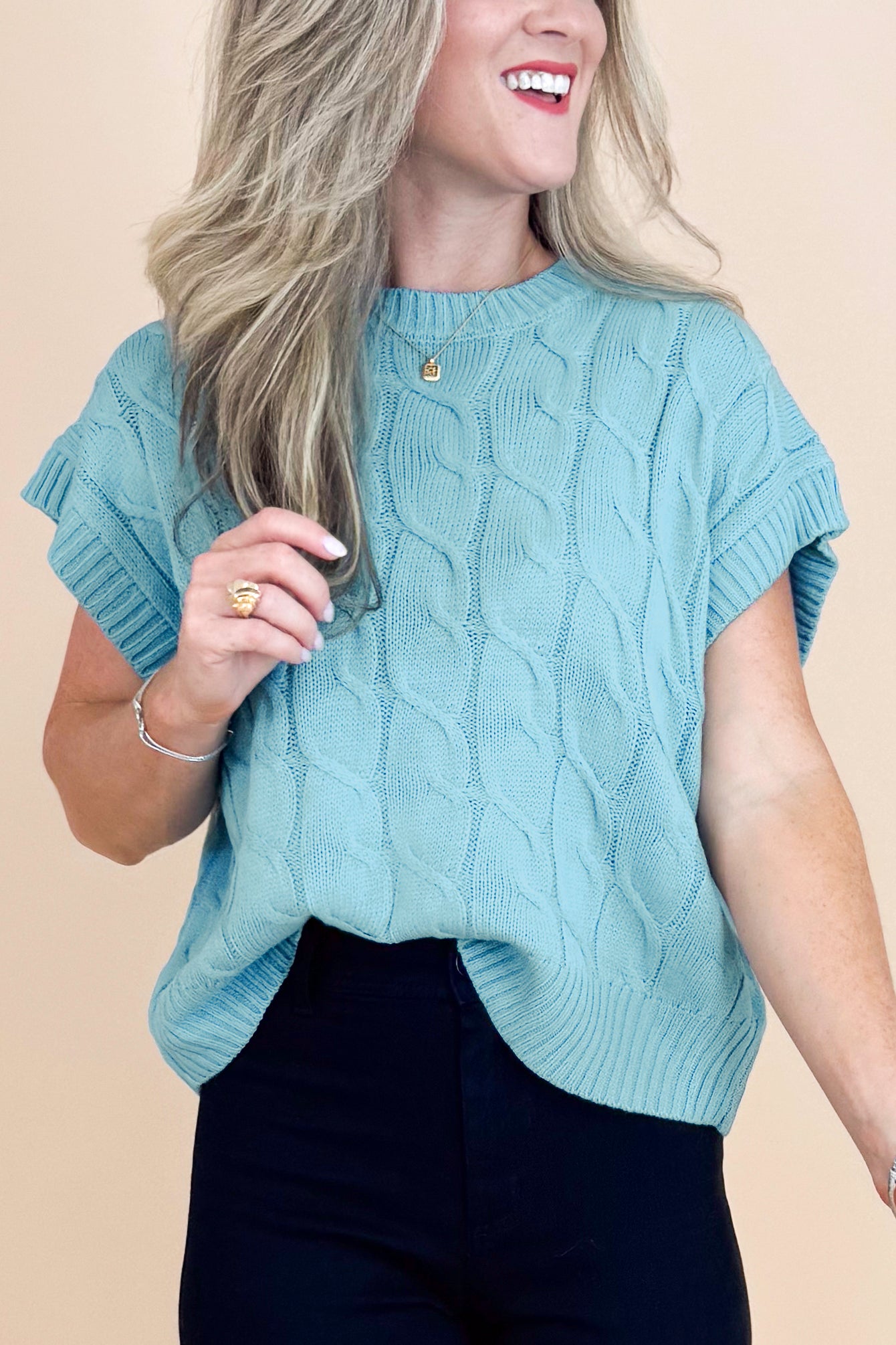 Woman wearing a light blue cable knit sweater against a beige background