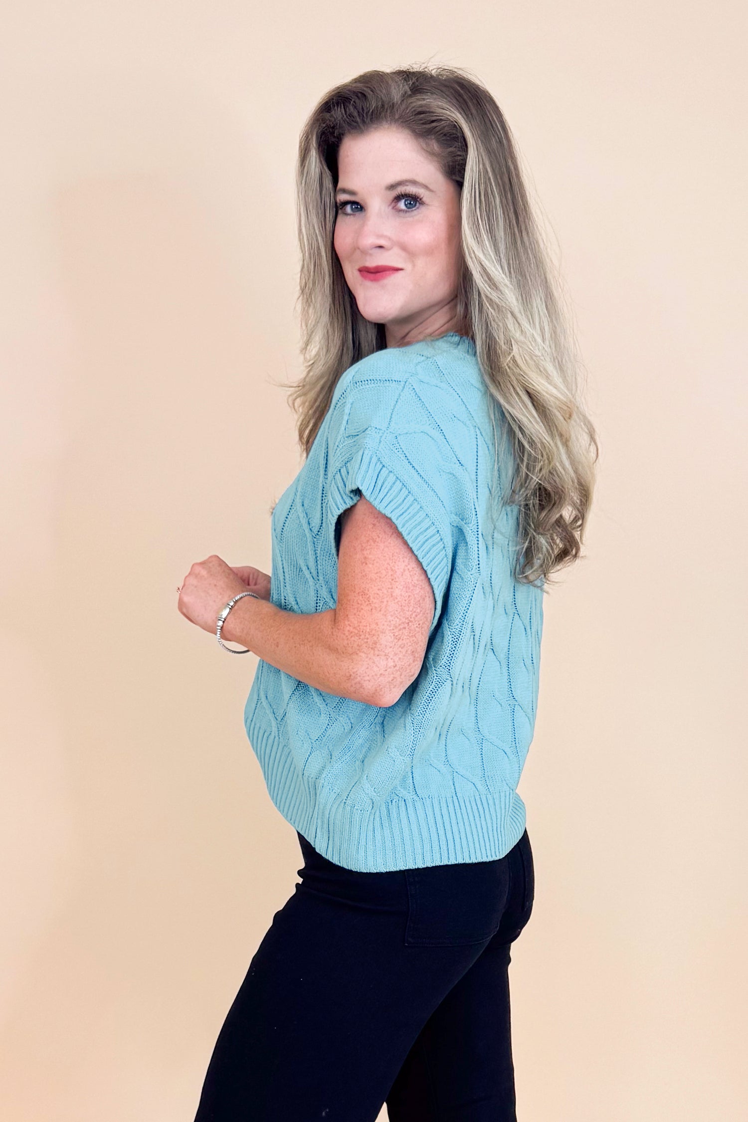 Woman wearing a light blue sweater over a black top against a beige background