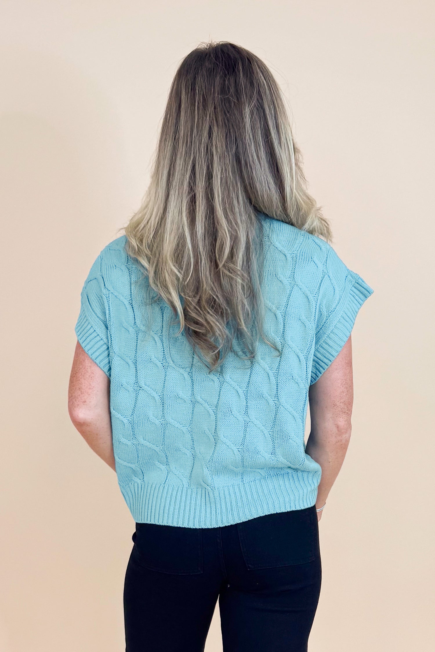 Person wearing a light blue knitted vest on a beige background