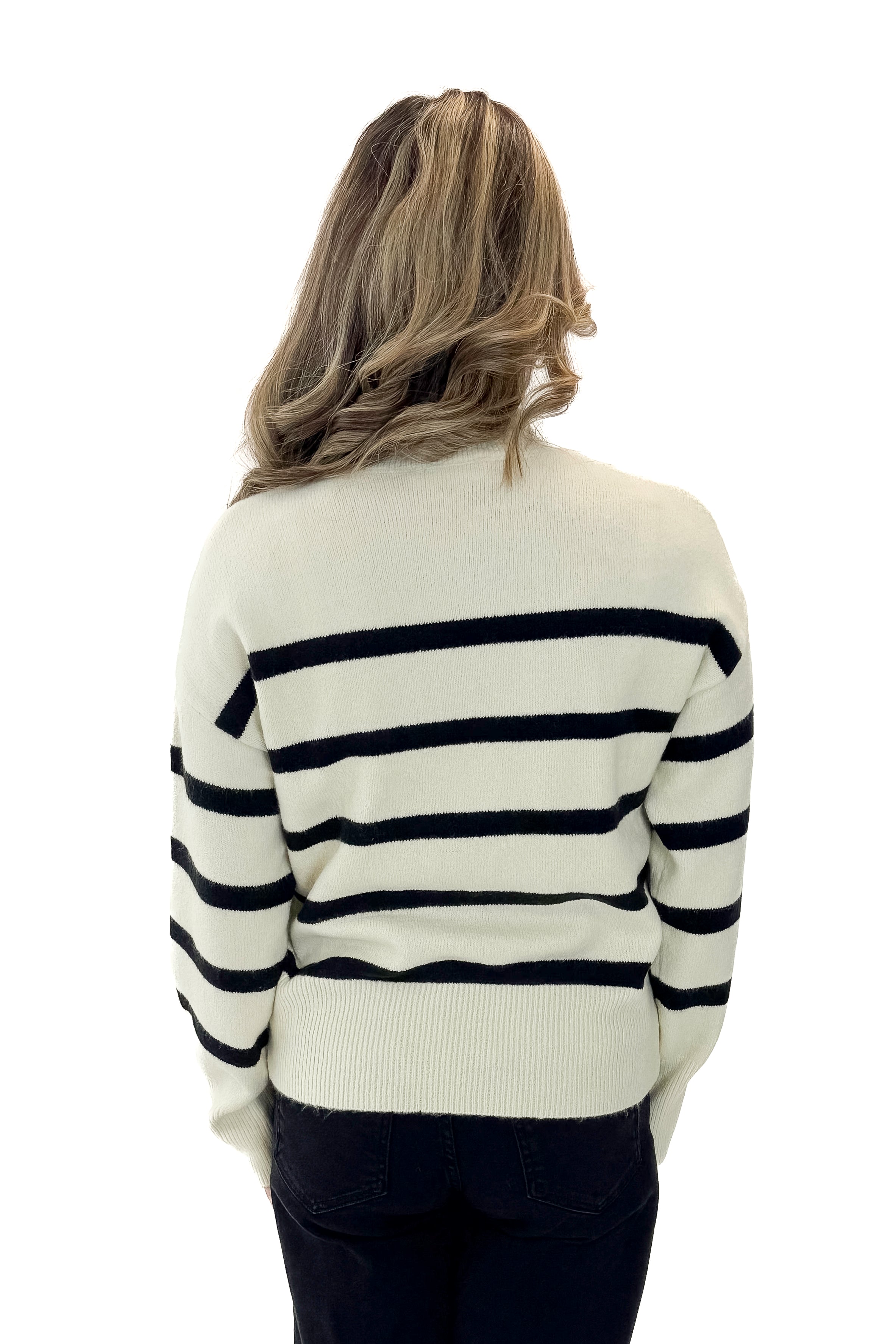 Back view of woman wearing Black & Cream Striped Mock Neck Sweater with jeans against white studio background.
