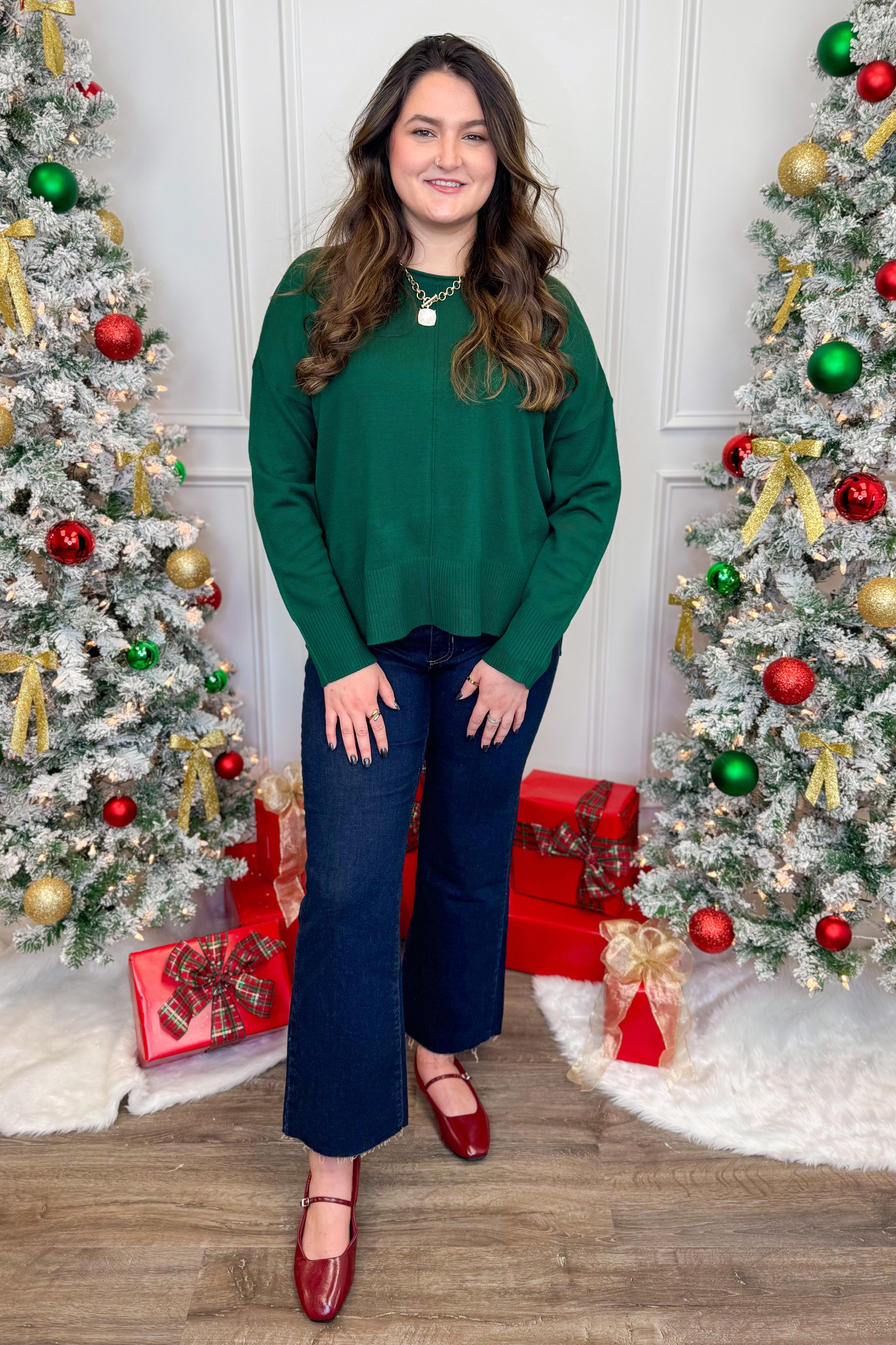 Front view of woman wearing green sweater and jeans with Christmas trees in the background.