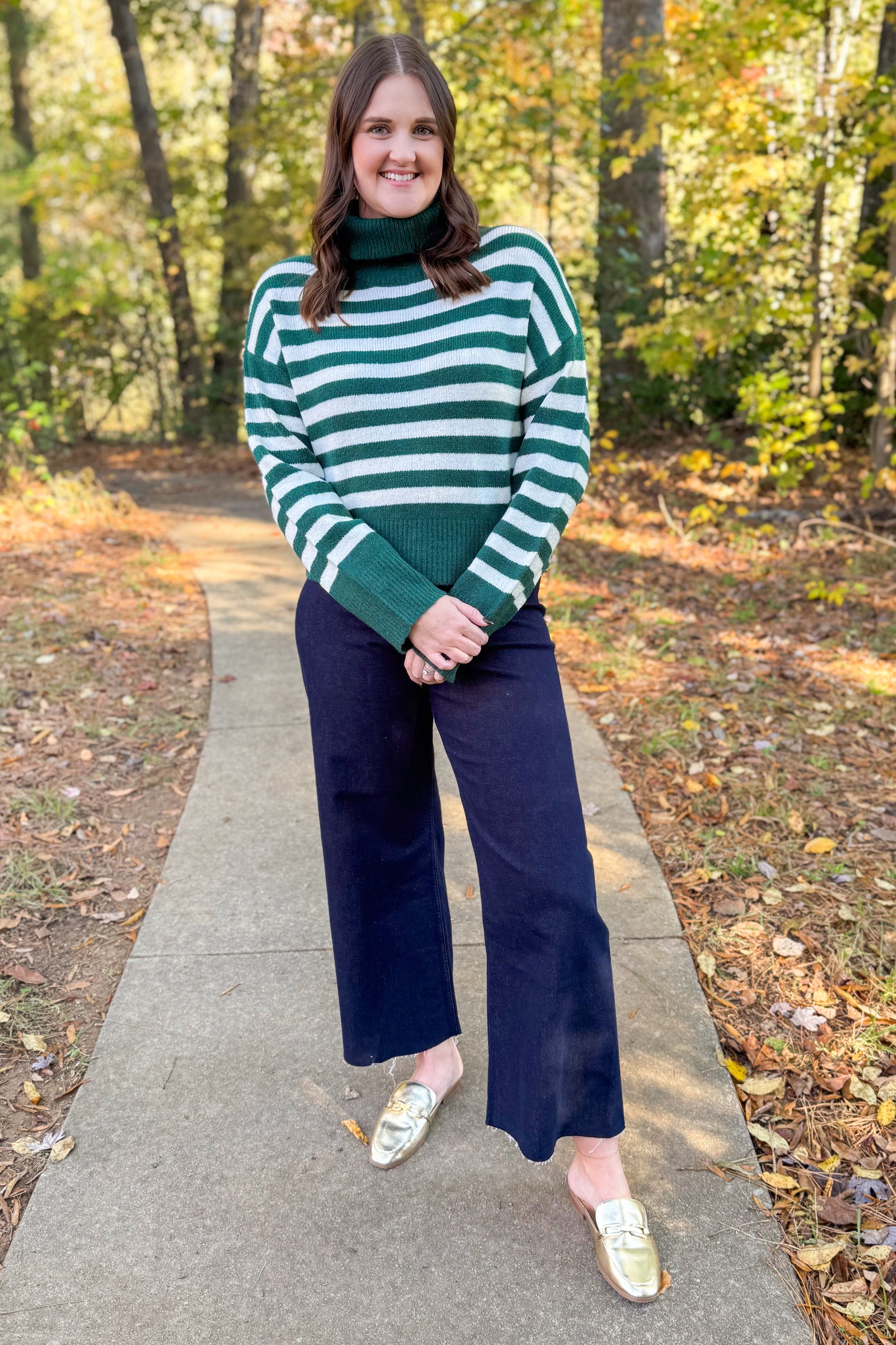 Front view of woman wearing Green & Cream Striped Turtleneck Sweater with jeans outside.