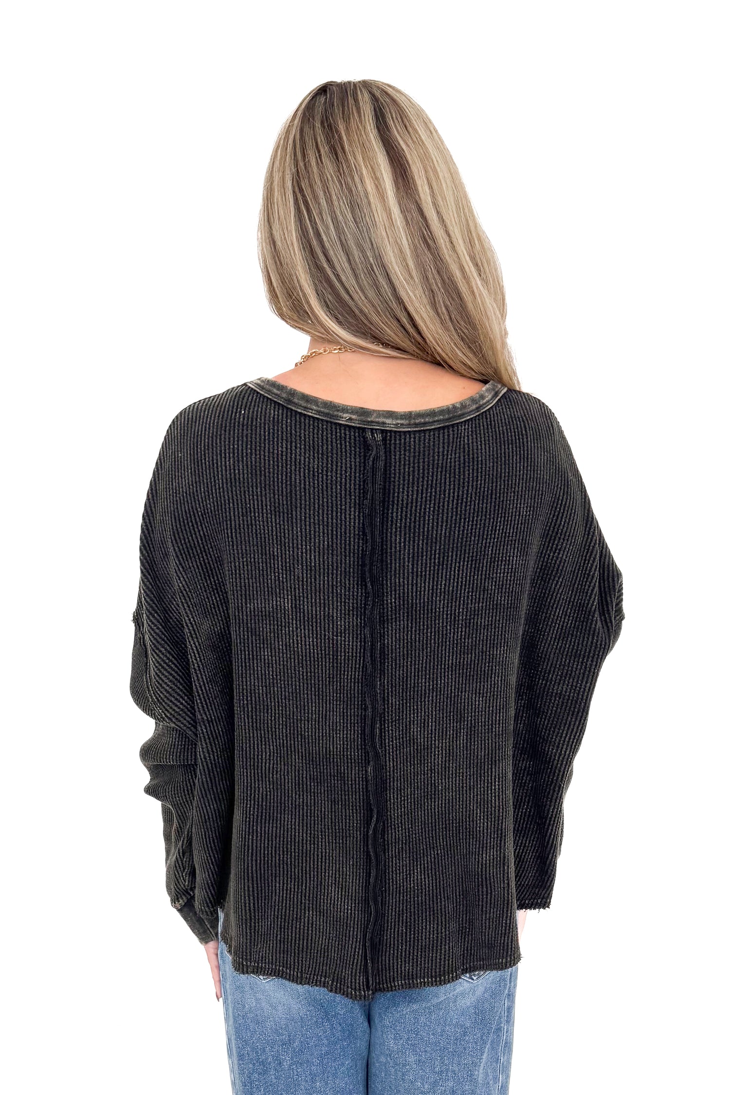 Back view of woman wearing washed black waffle top with jeans against white studio background.
