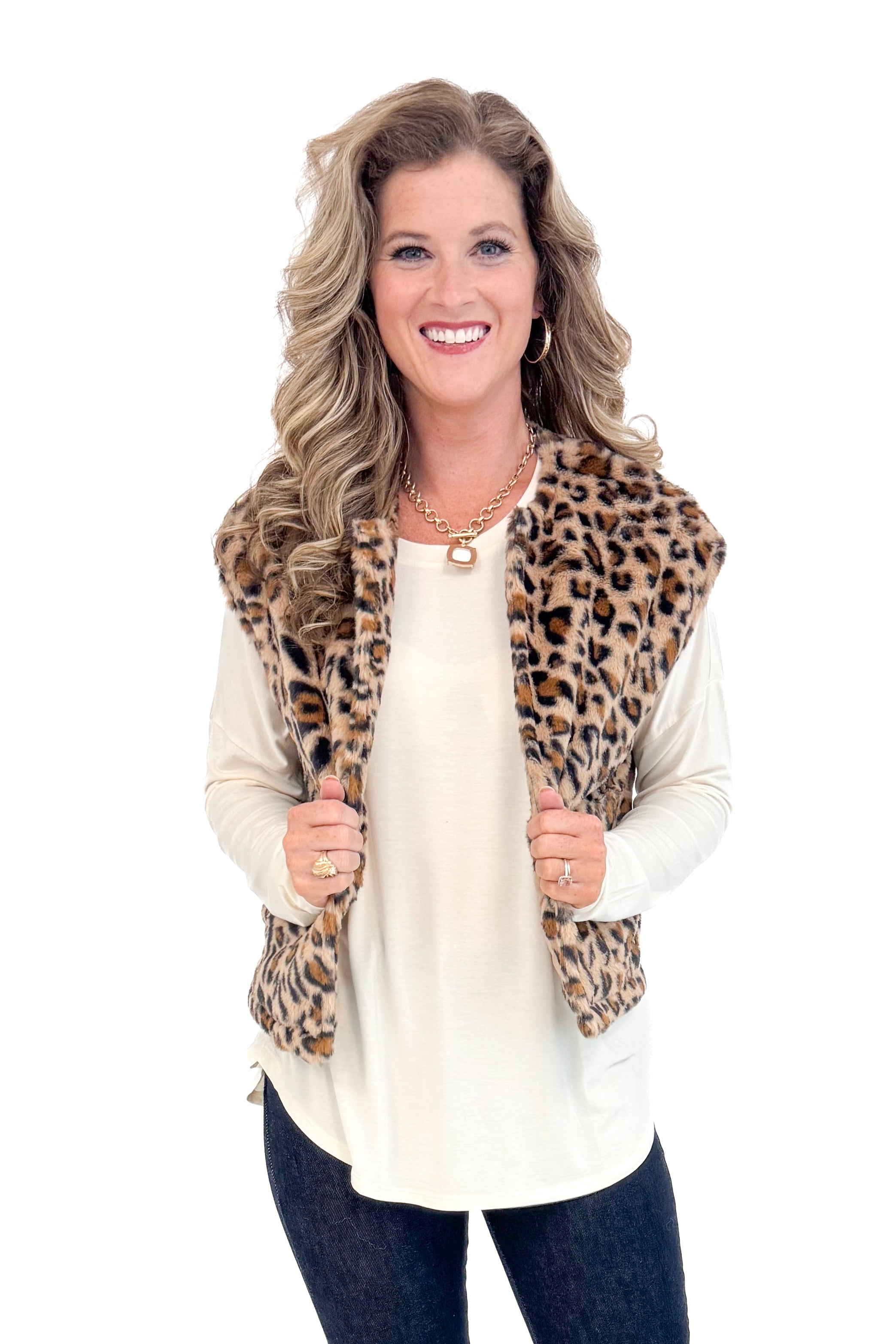 Front view of woman with cream long sleeve curve hem top and blue jeans and leopard jacket.