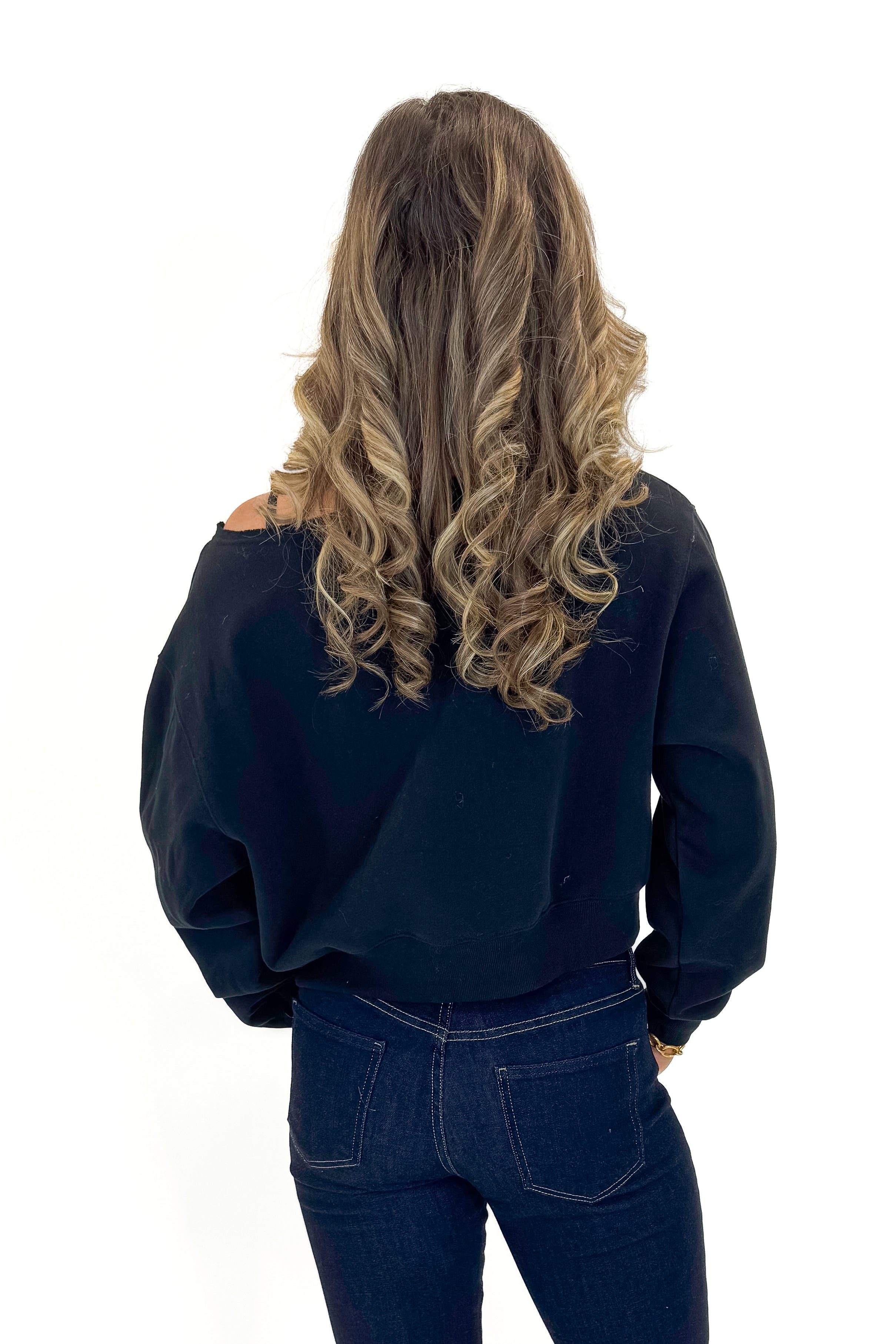 Back view of woman wearing Black Boatneck Banded Sweatshirt with jeans against white studio background.
