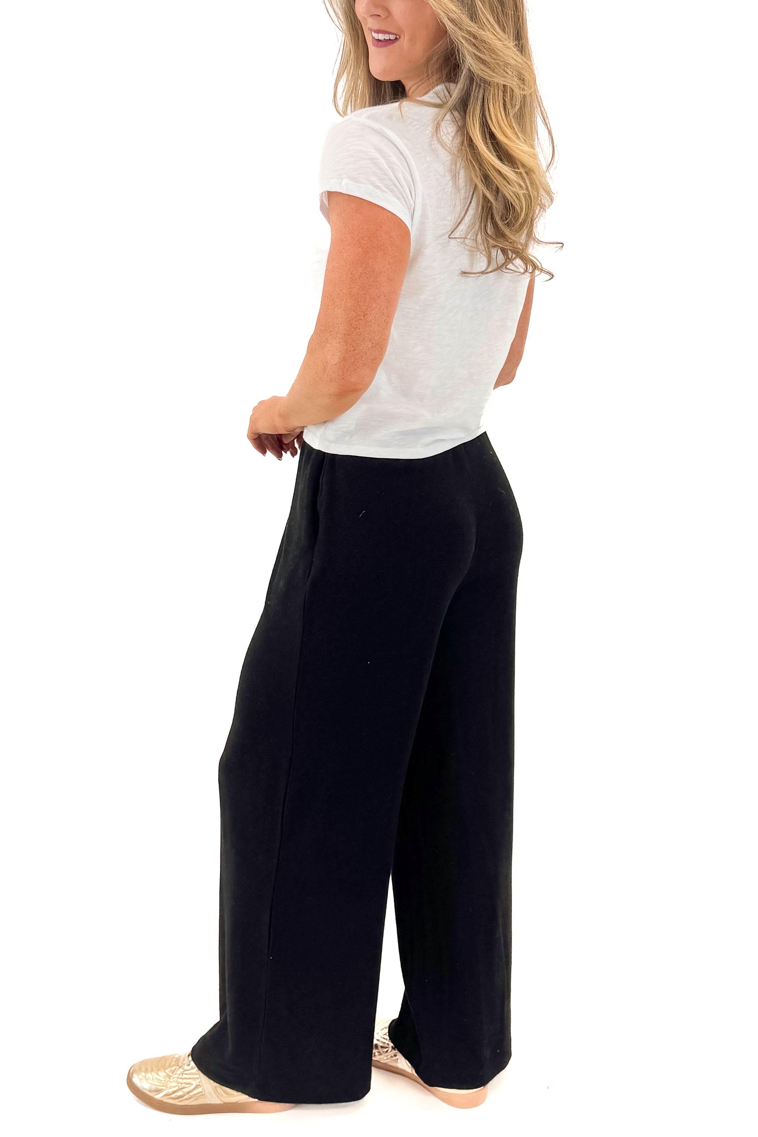 Side view of woman wearing Black Brushed Wide Leg Sweatpants with white top against white studio background.