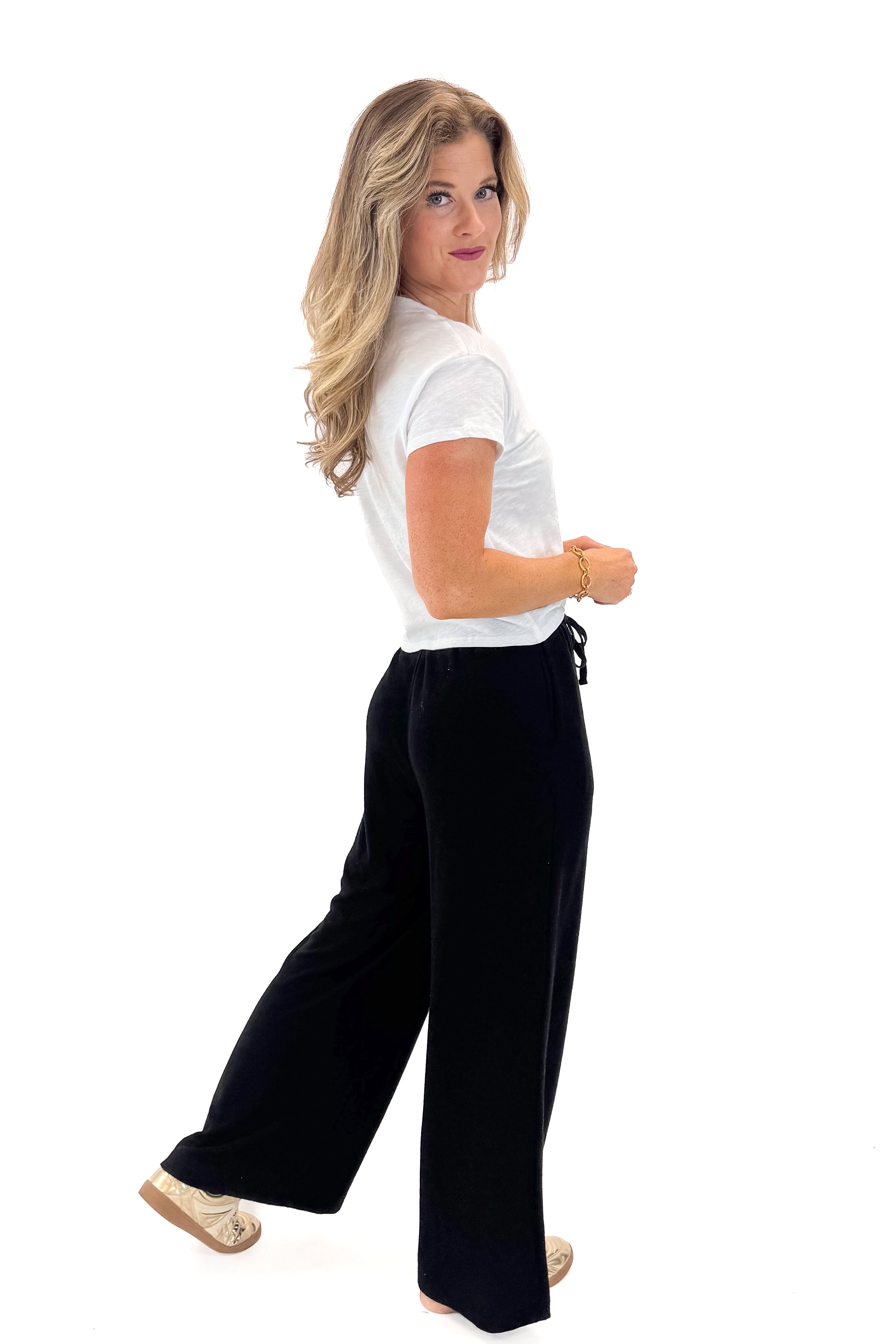 Side view of woman wearing Black Brushed Wide Leg Sweatpants with white top against white studio background.