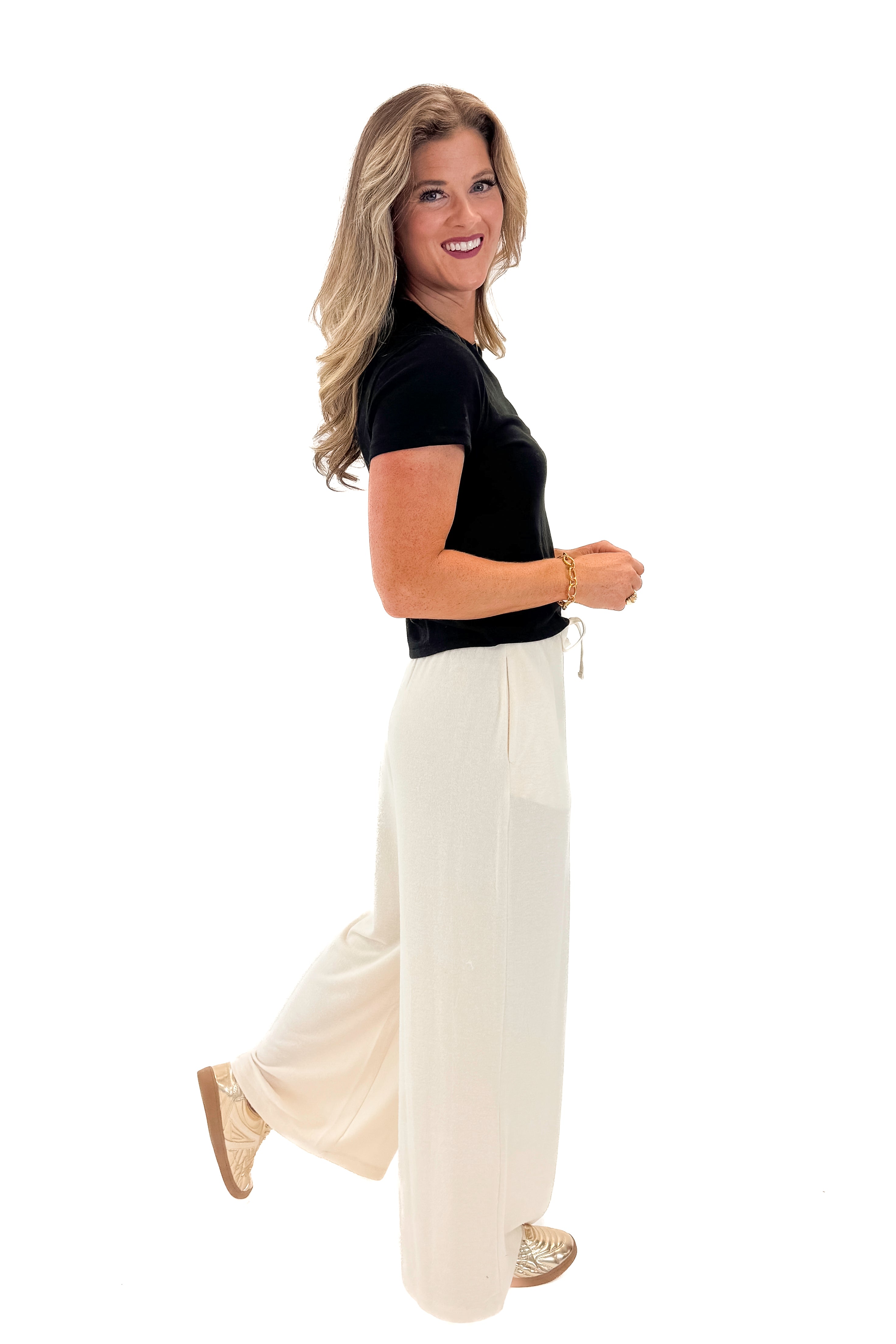 Side view of woman wearing black top with Cream Brushed Wide Leg Sweatpants against white studio background.