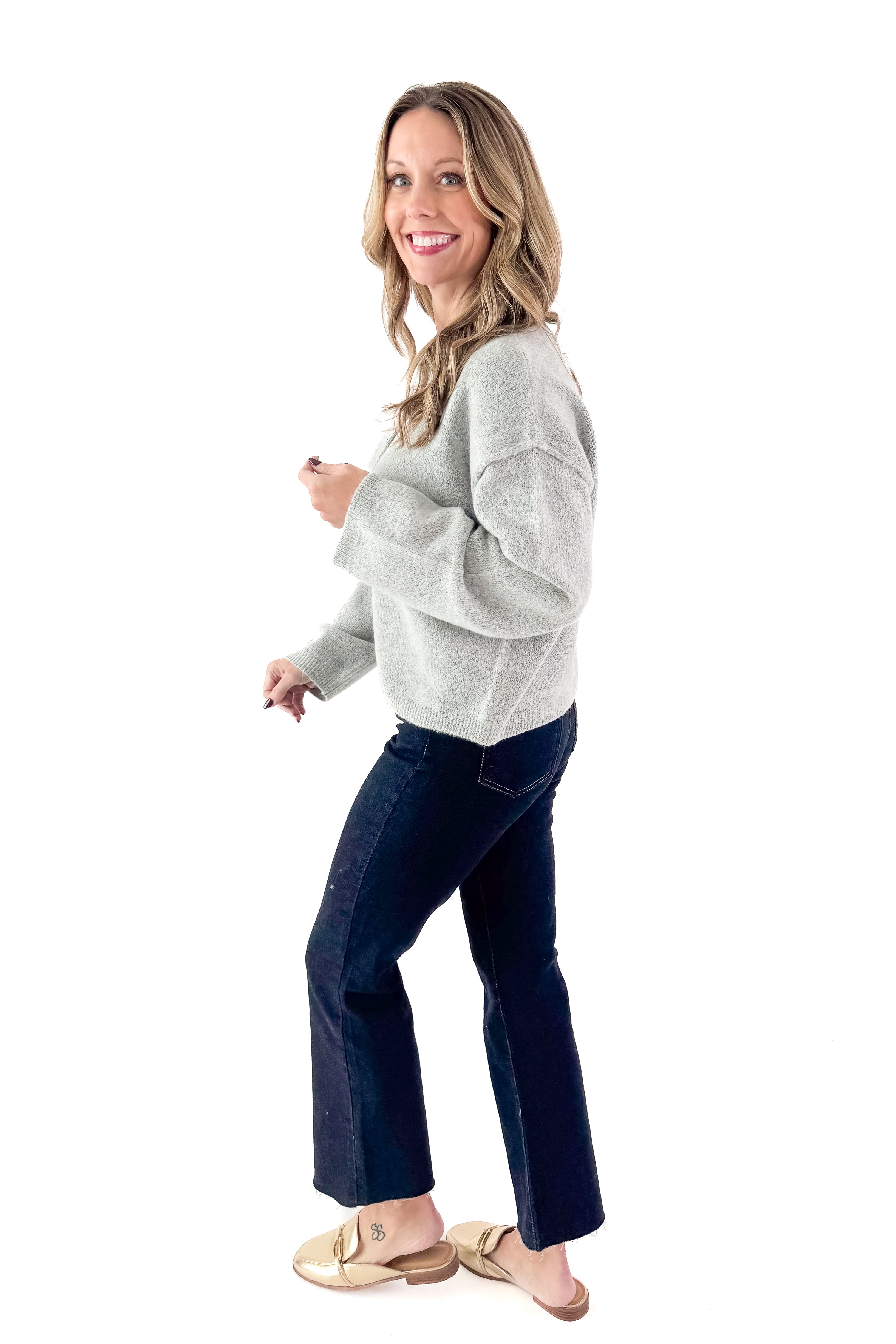 Side view of woman wearing Heather Grey Button Up Cardigan with jeans against white studio background.