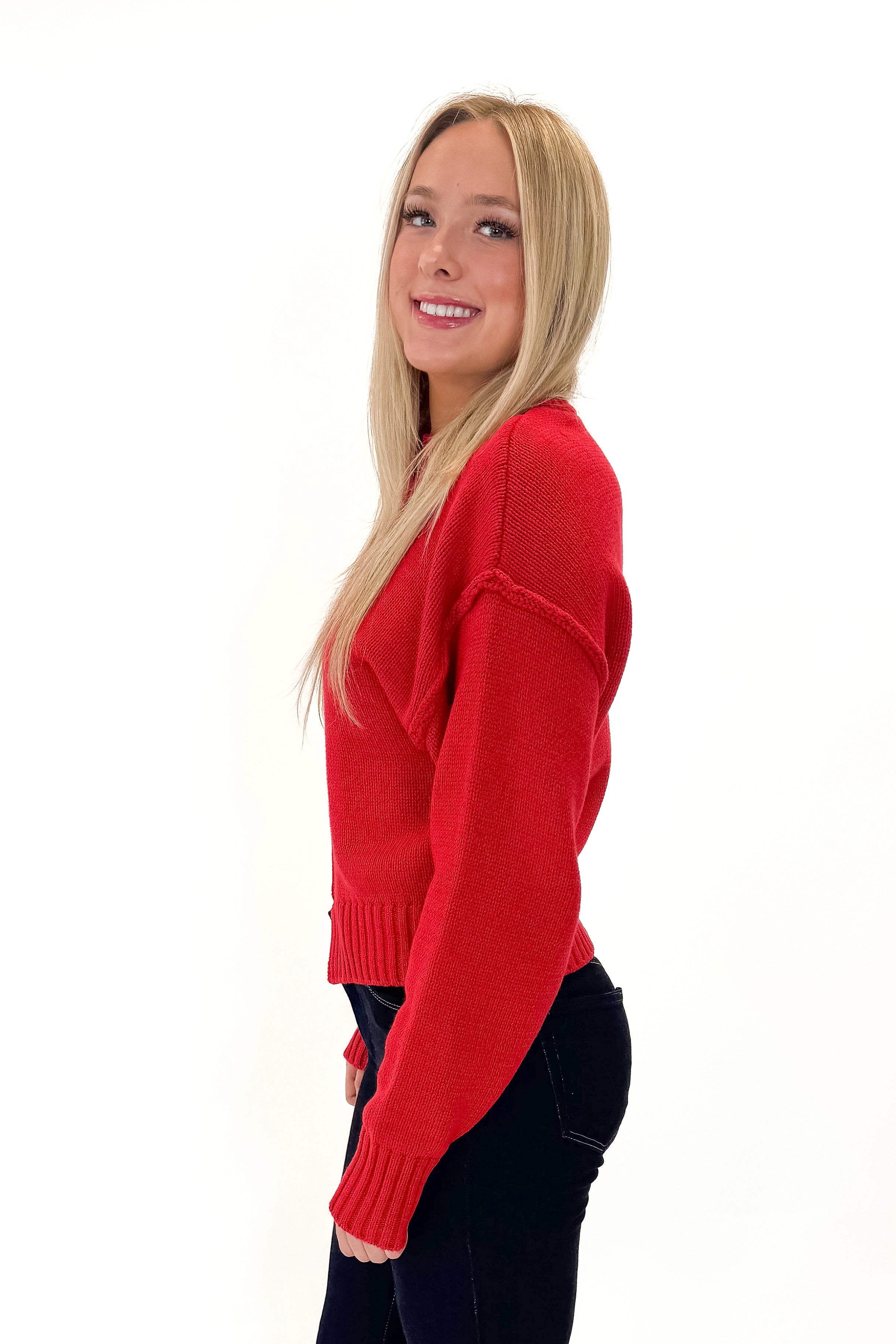 Side view of woman wearing Red Seam Split Detail Sweater with jeans against white studio background.