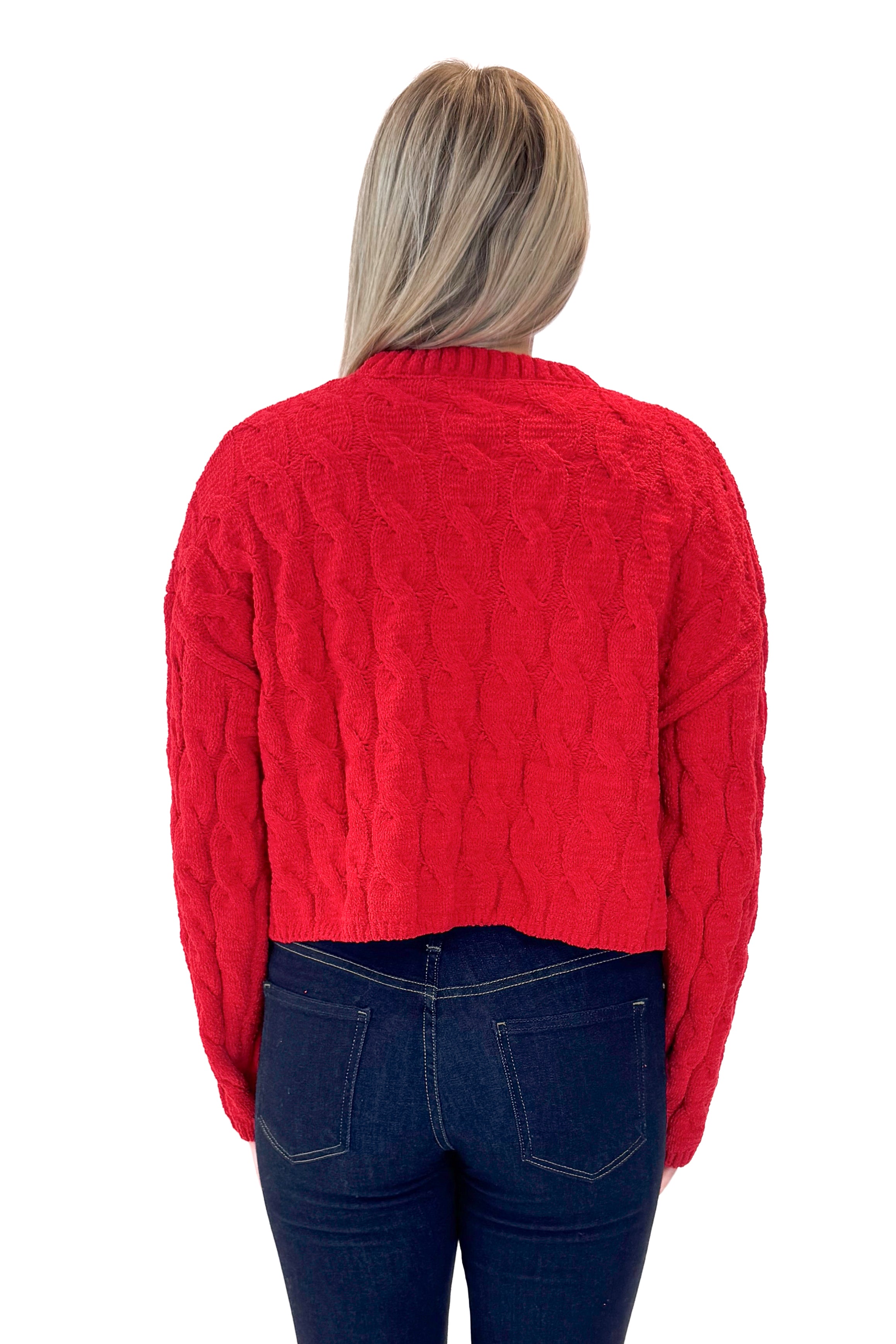 Back view of woman wearing Red Textured Cable Knit Sweater with skirt against white studio background.