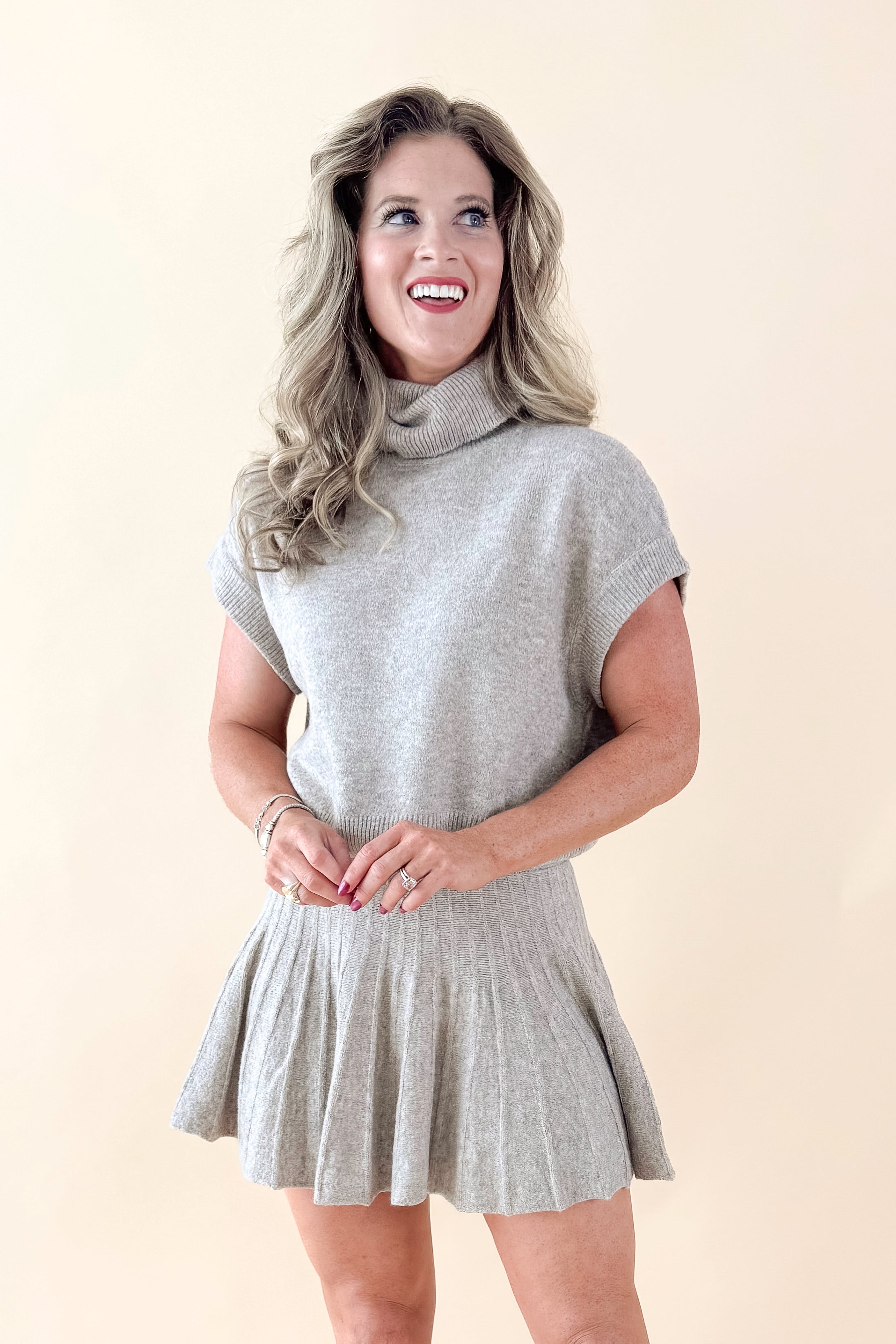Front view of woman wearing Taupe Pleated Sweater Skirt with matching sweater against tan studio background.