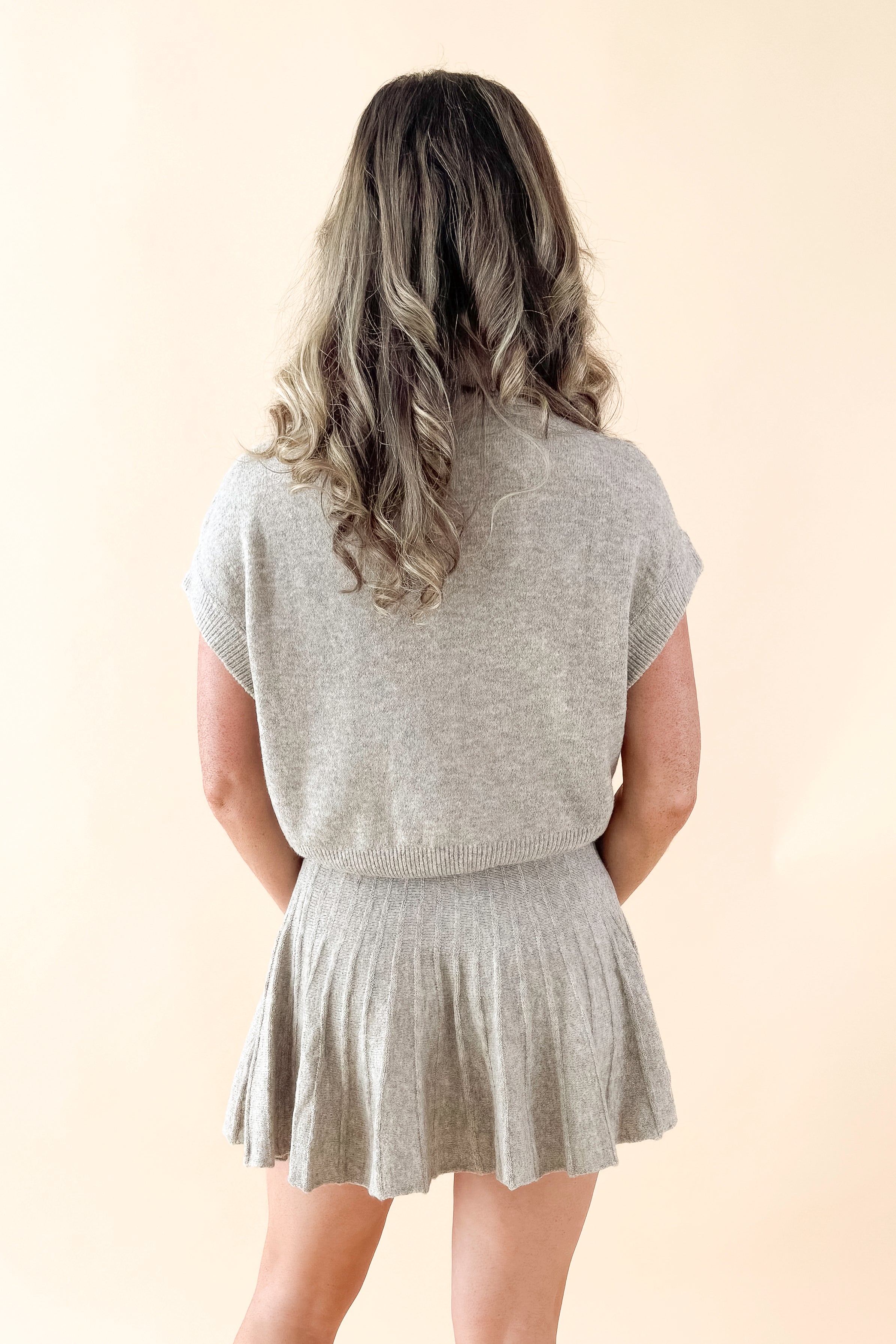 Back view of woman wearing Taupe Mock Neck Short Sleeve Sweater with matching skirt against tan studio background.