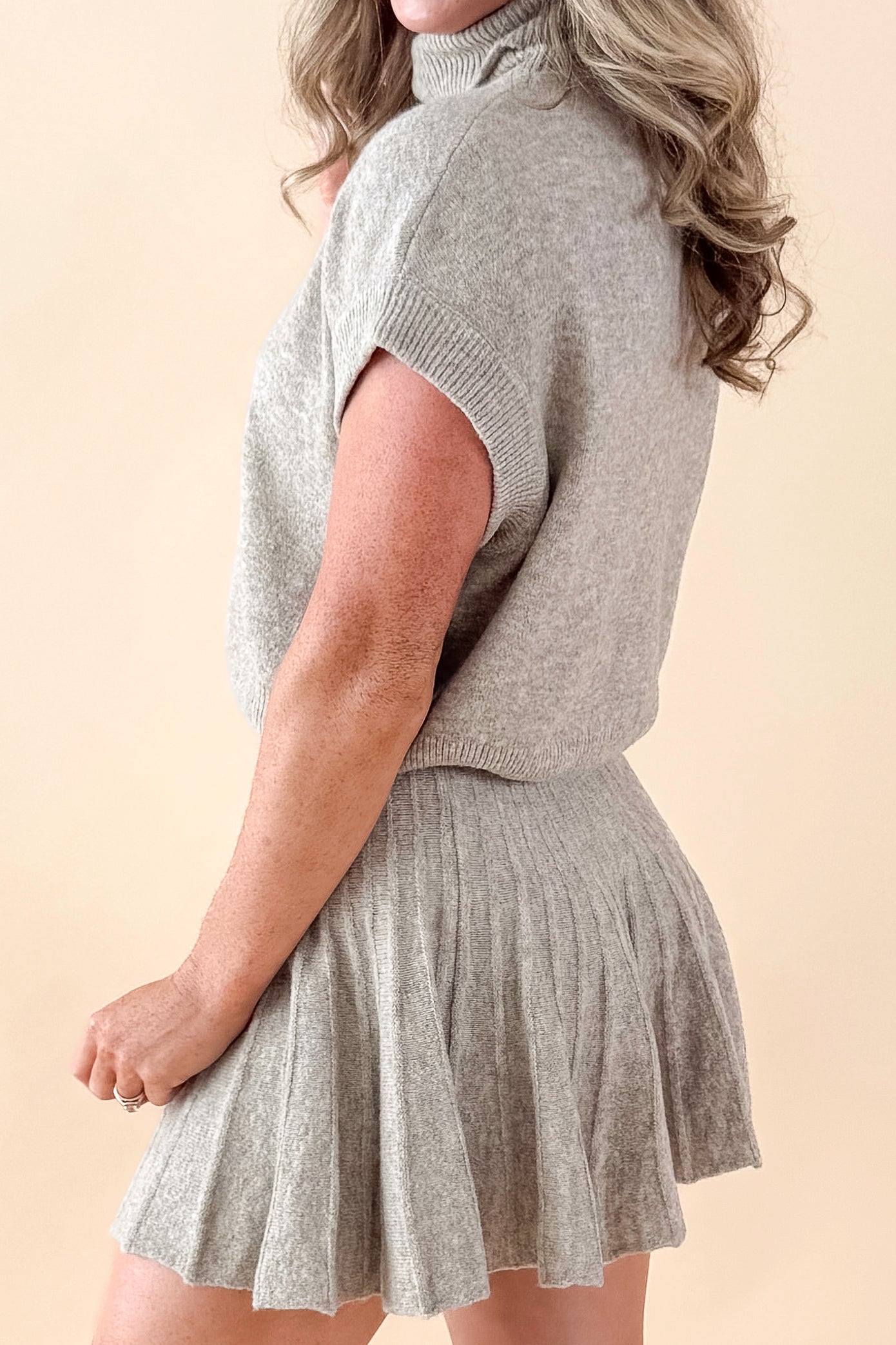 Side view of woman wearing Taupe Mock Neck Short Sleeve Sweater with matching skirt against tan studio background.