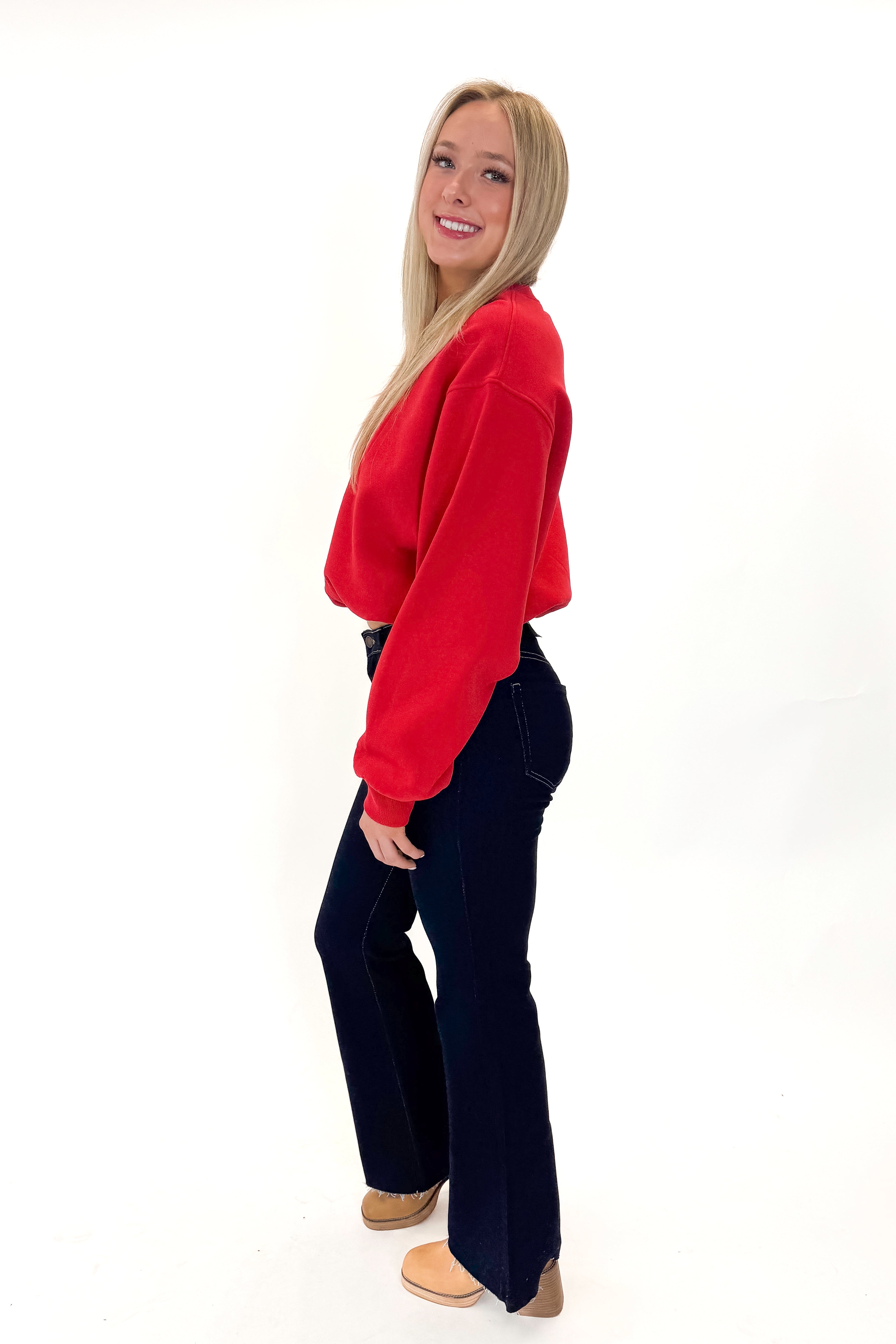Side view of woman wearing Red Elastic Hem Sweatshirt with jeans against white studio background.