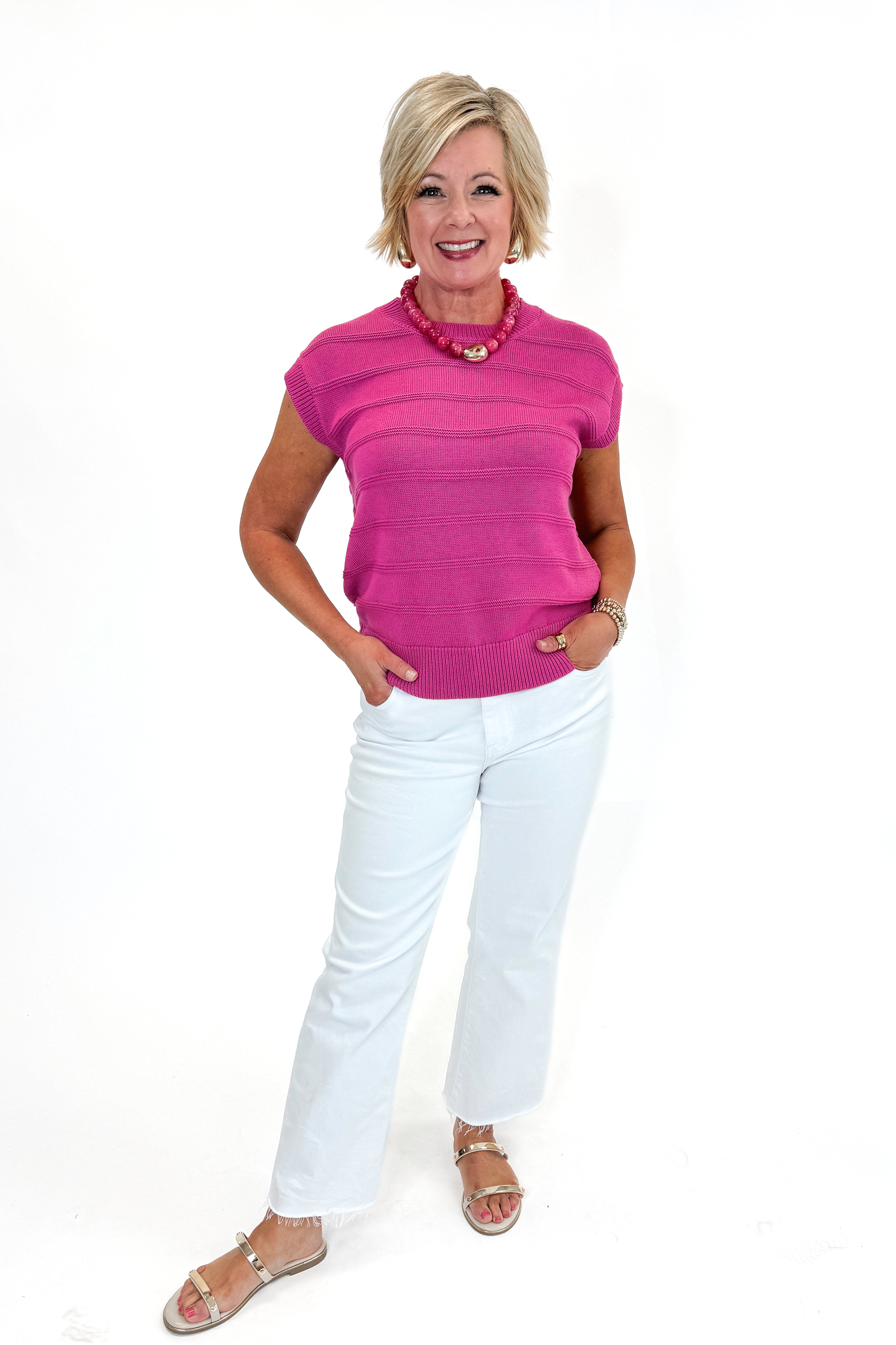 Front view of woman wearing Fuchsia Textured Detail Sleeveless Sweater with jeans against white studio background.