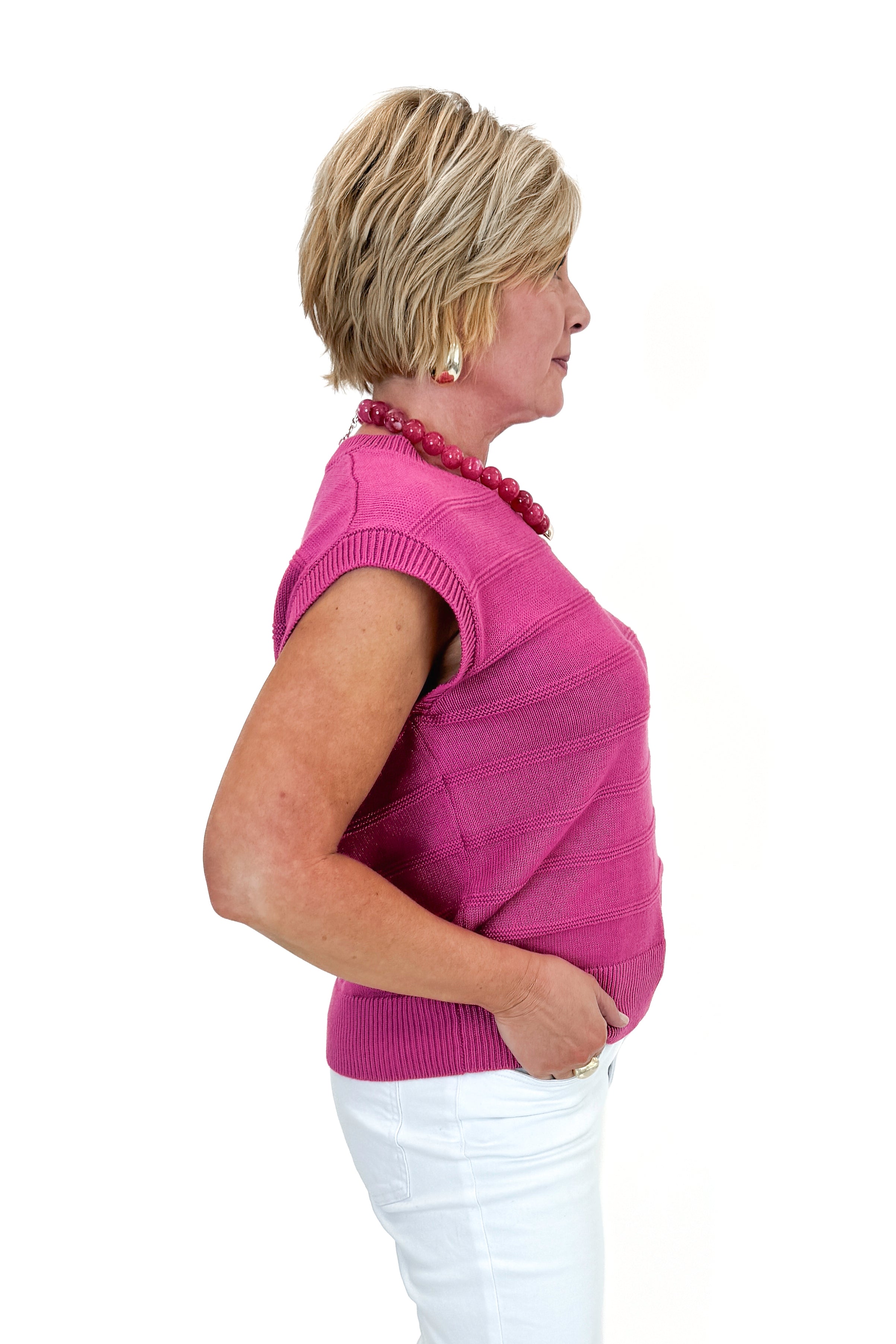 Side view of woman wearing Fuchsia Textured Detail Sleeveless Sweater with jeans against white studio background.