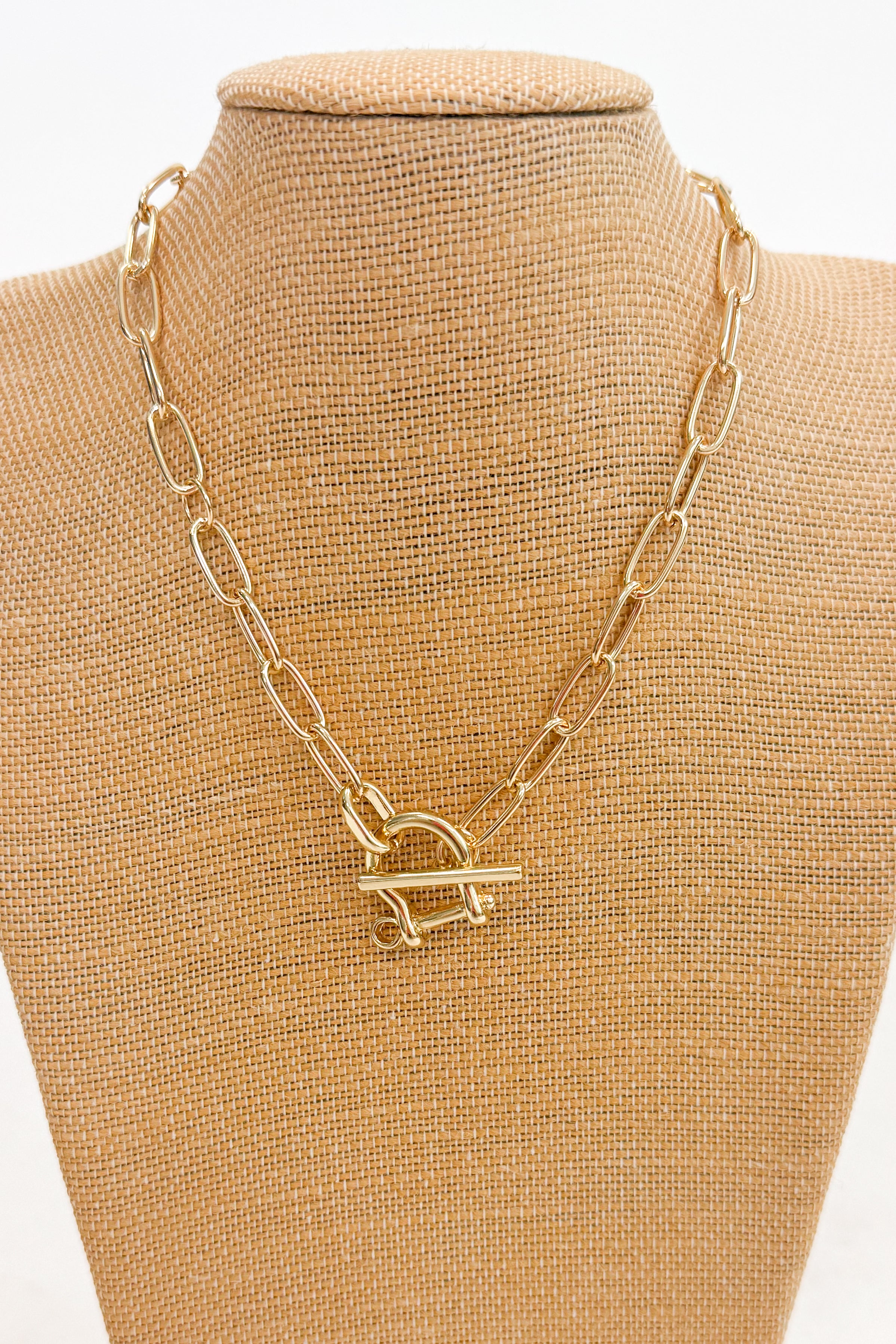 Gold chain necklace with a horsebit pendant on a beige mannequin bust.