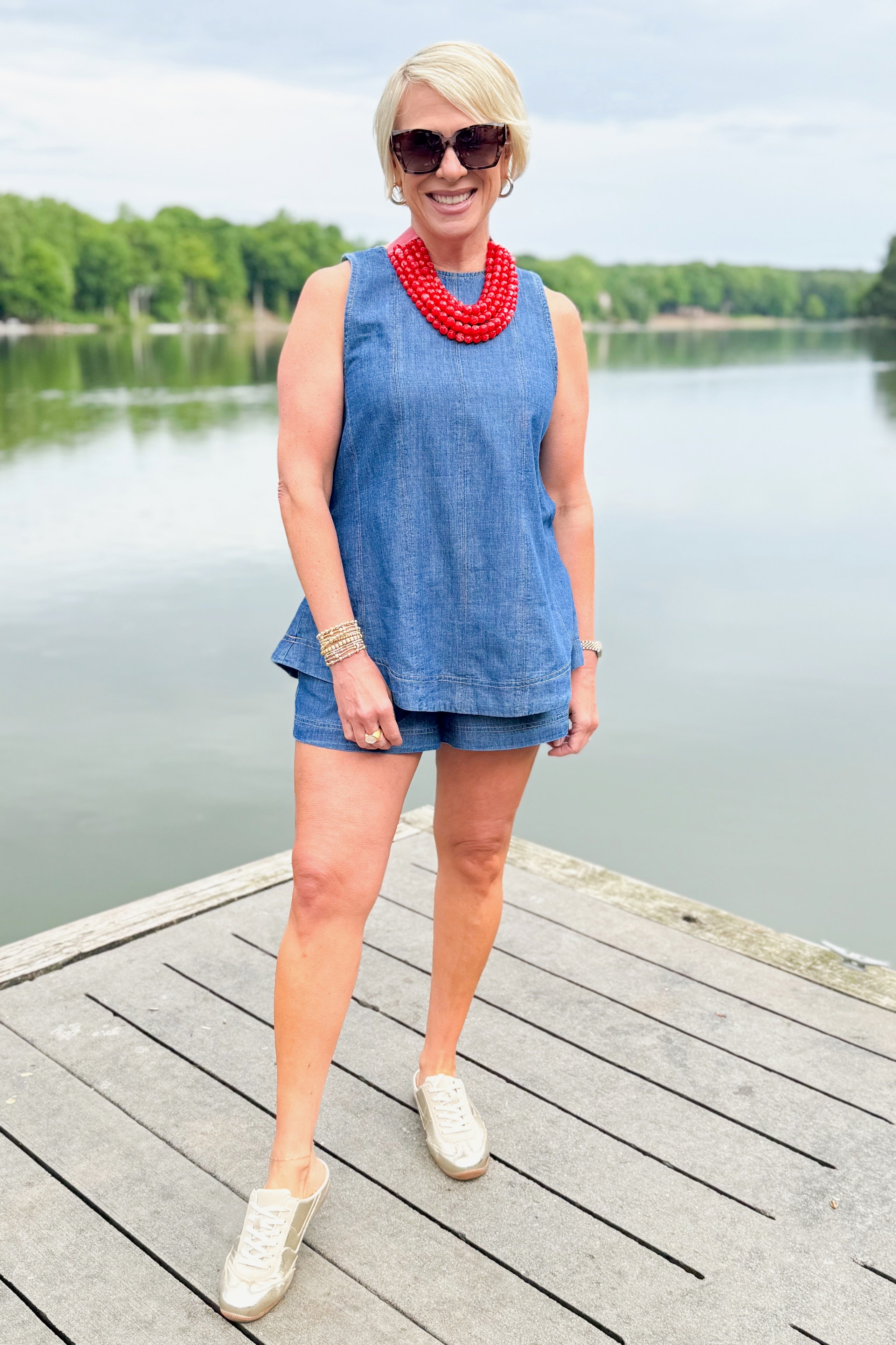 Front view of woman wearing Swagger Boutique’s Denim Seam Detail Swing Tank with matching Denim Seam Detail Shorts and sneakers outside at the lake.