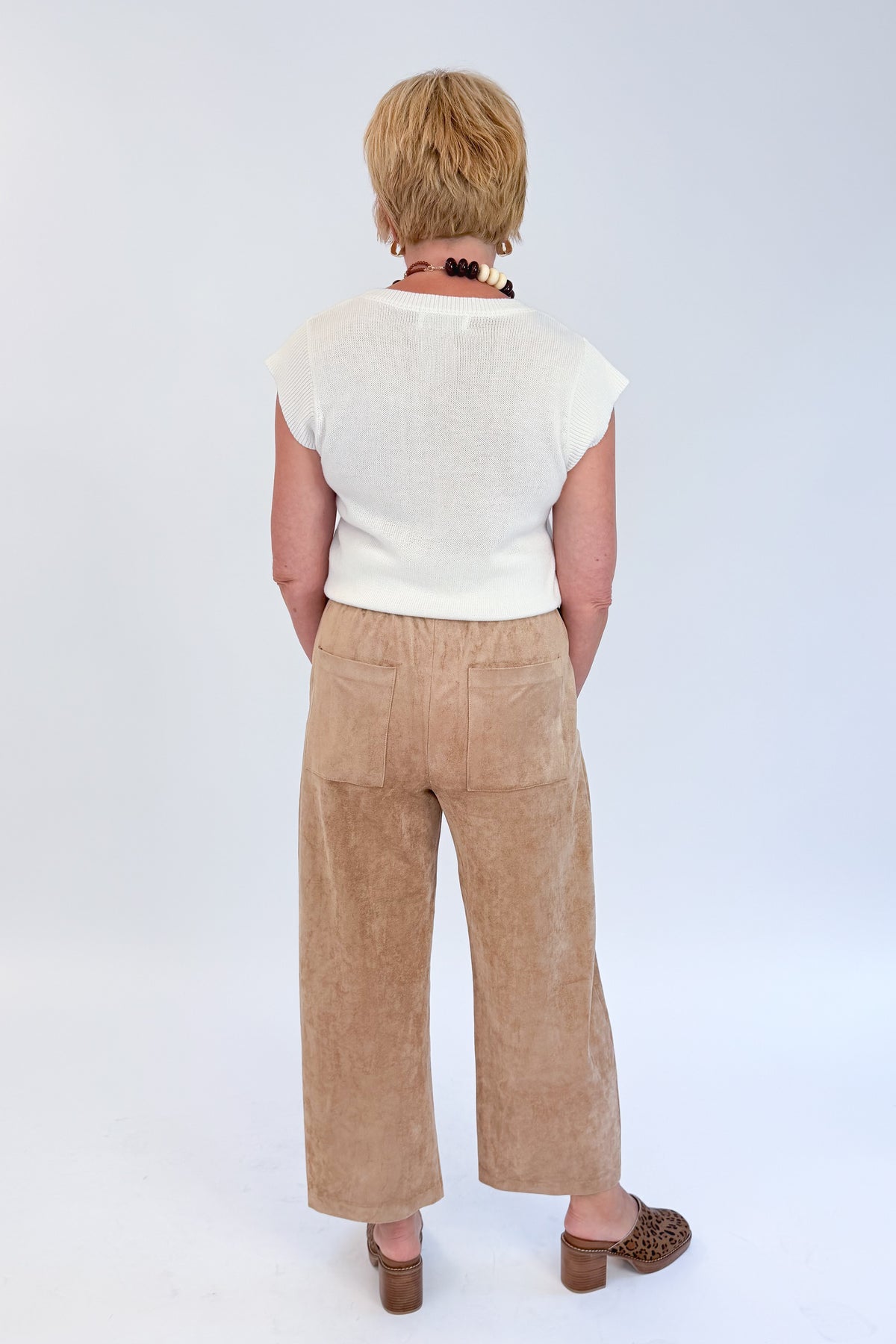 Back view of woman wearing Swagger Boutique’s Light Sand Drift Suede Pants by Z Supply with sweater against white studio background.