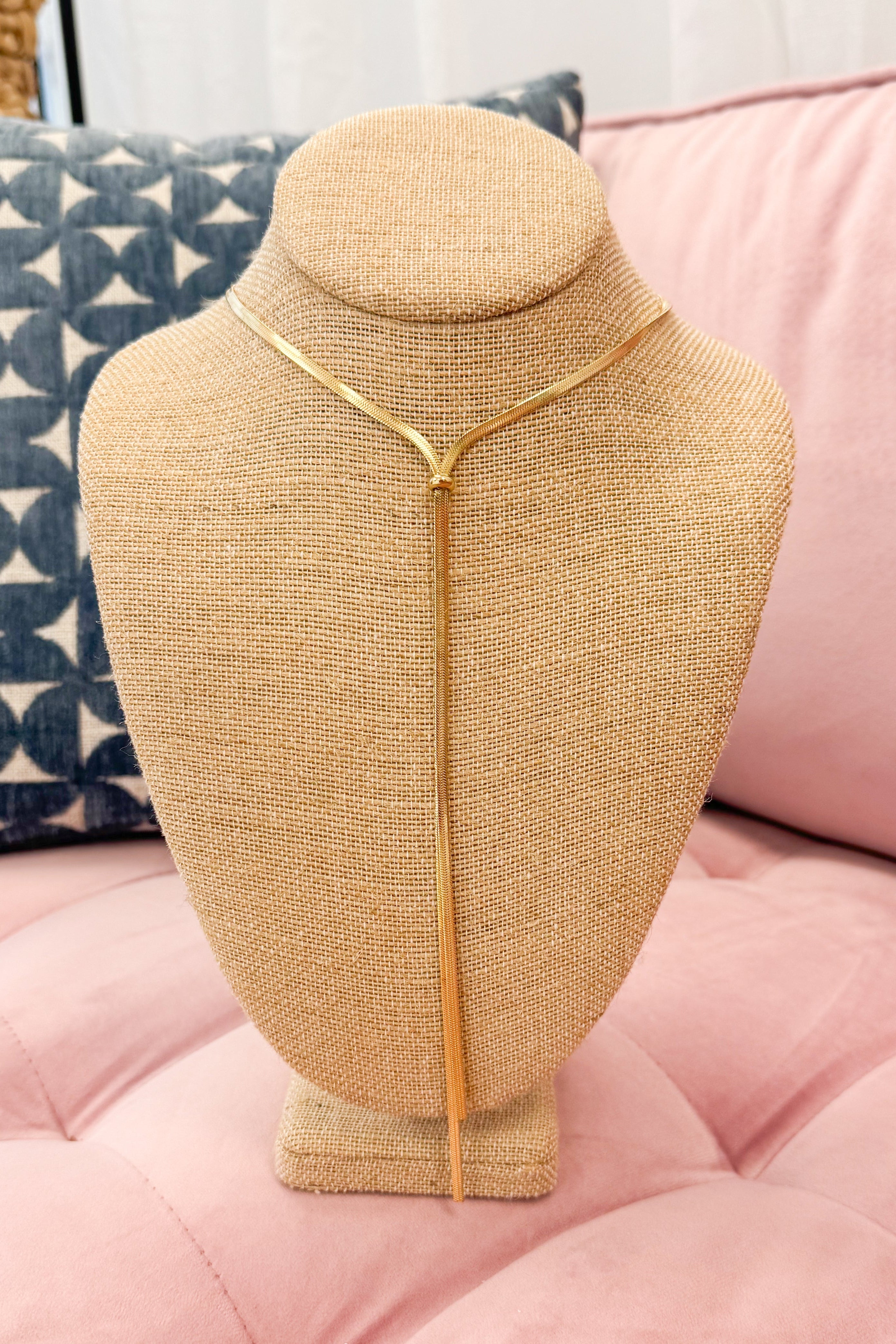 Gold necklace on a mannequin bust against a pink and blue patterned background