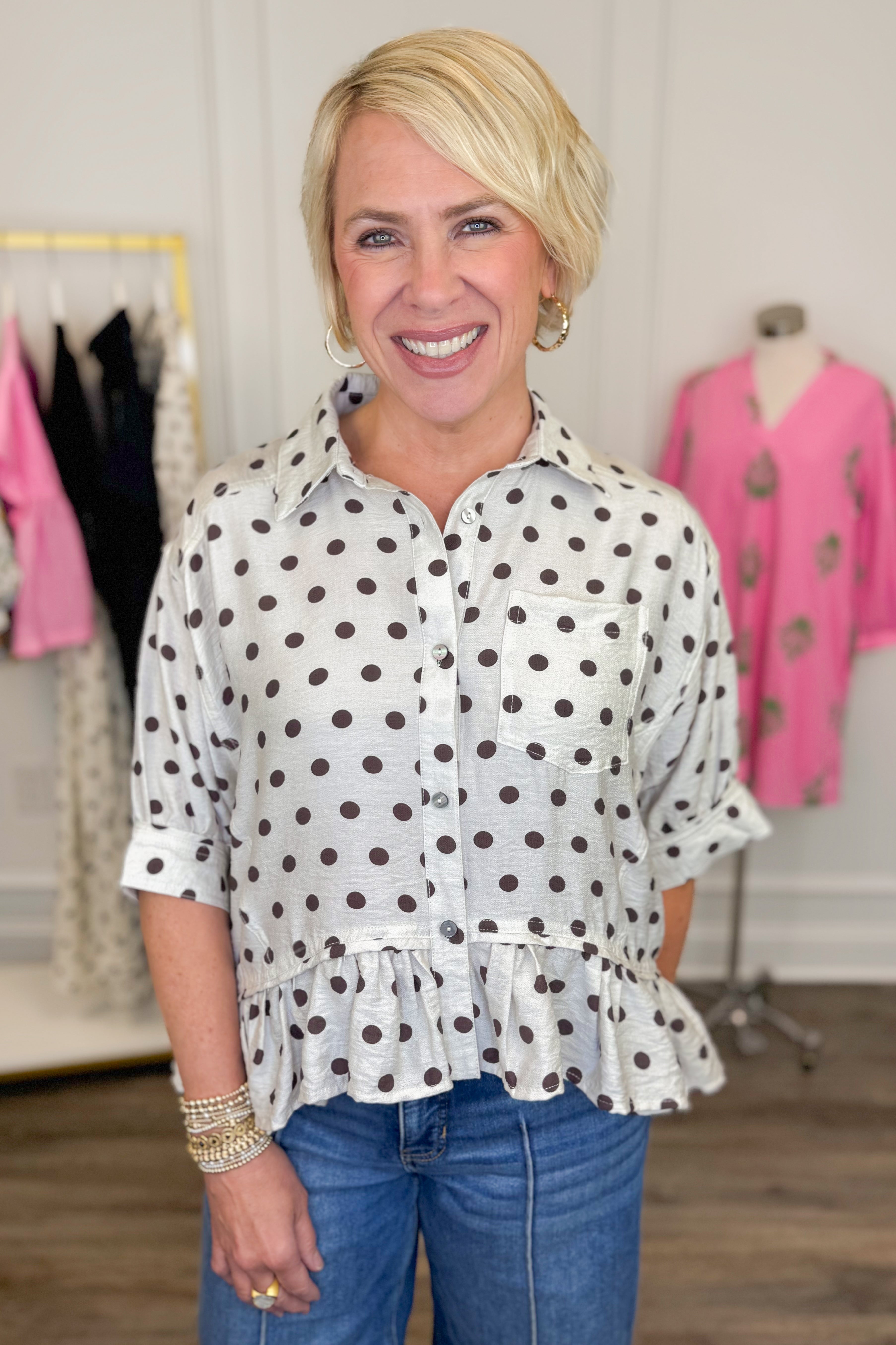 Front view of woman wearing Swagger Boutiqueβs Cream & Brown Polka Dot Peplum Top by Entro with jeans with clothes around her.