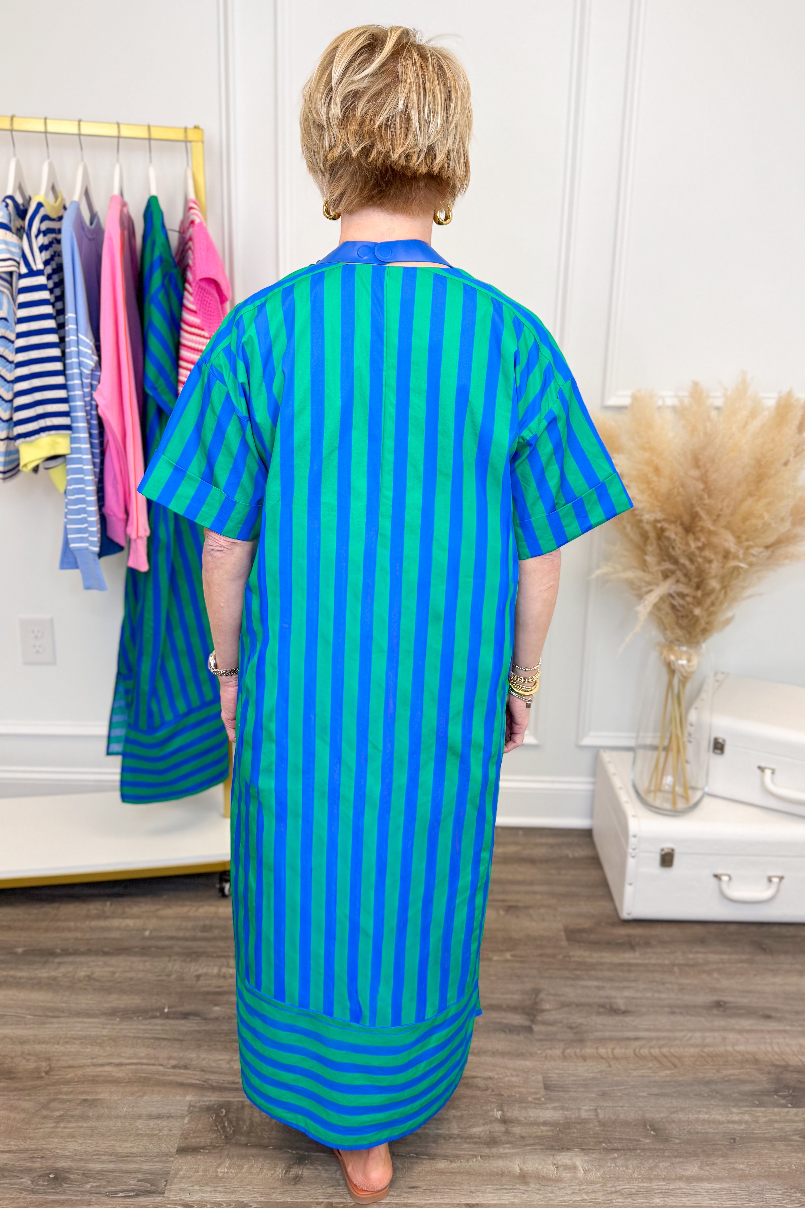Back view of woman wearing striped dress with blue necklace with clothes in background.