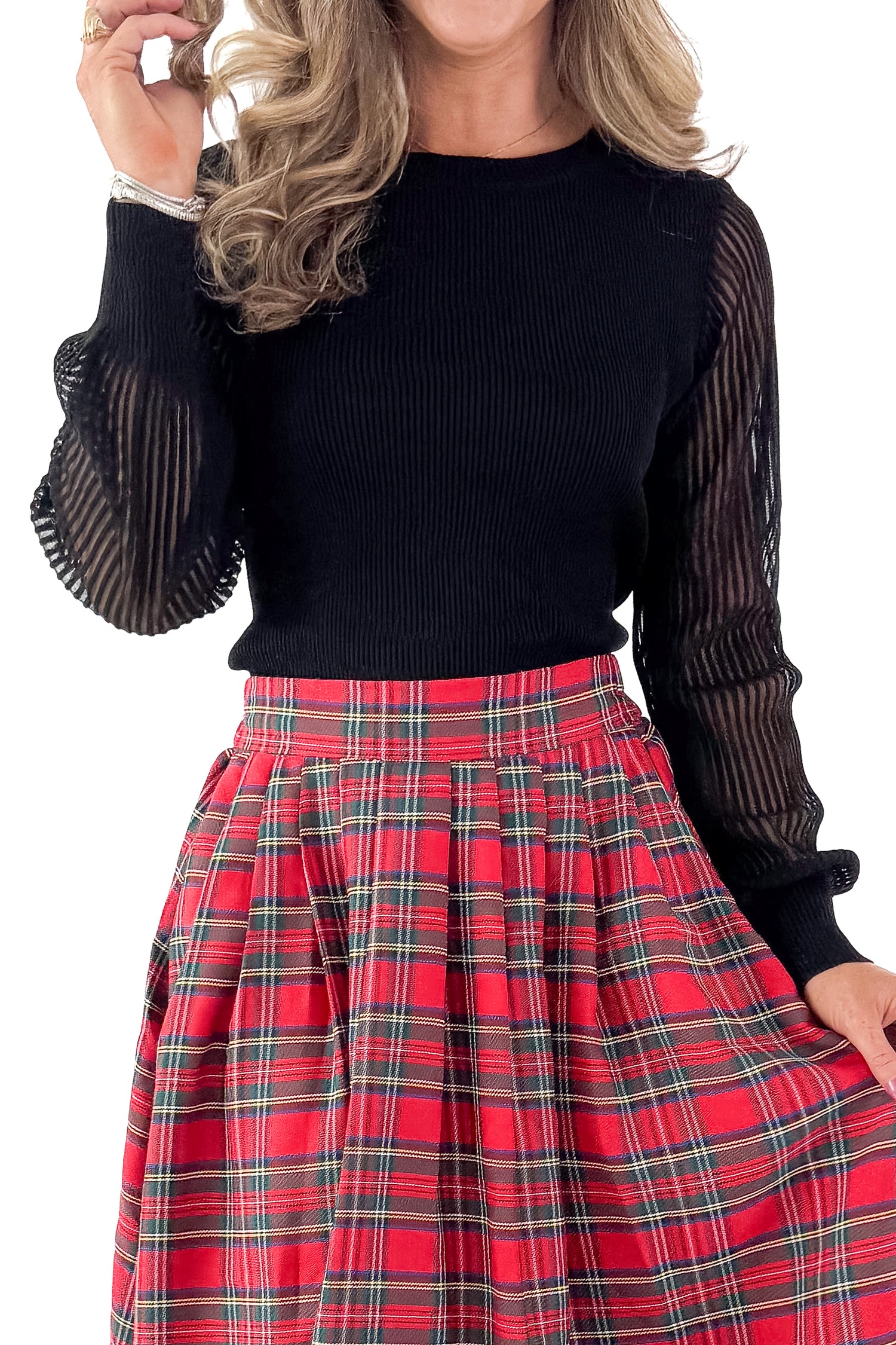 Front detail view of woman wearing black sheer sleeve sweater with red skirt against white studio background.