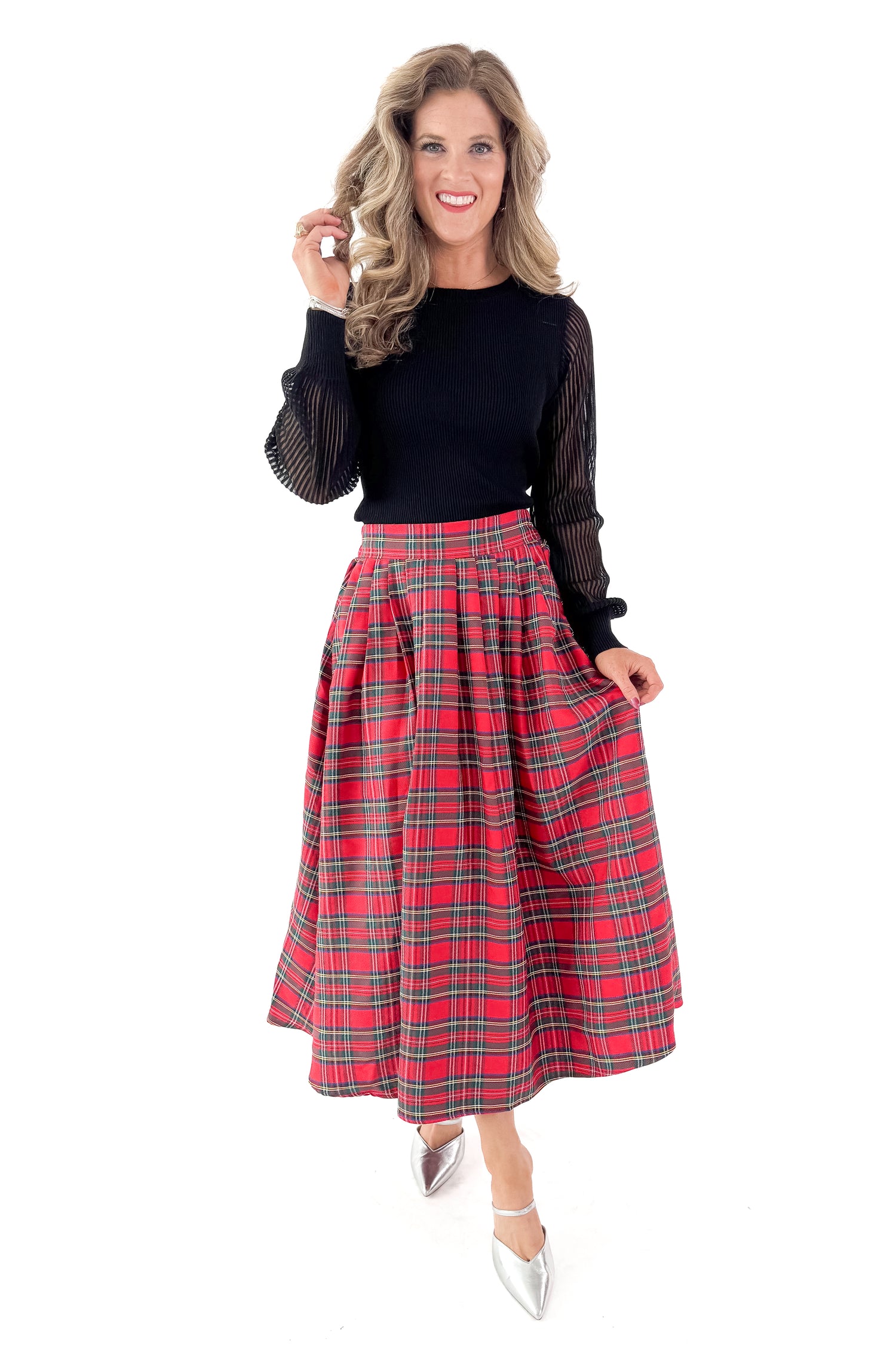 Front view of woman wearing black sheer sleeve sweater with red skirt against white studio background.