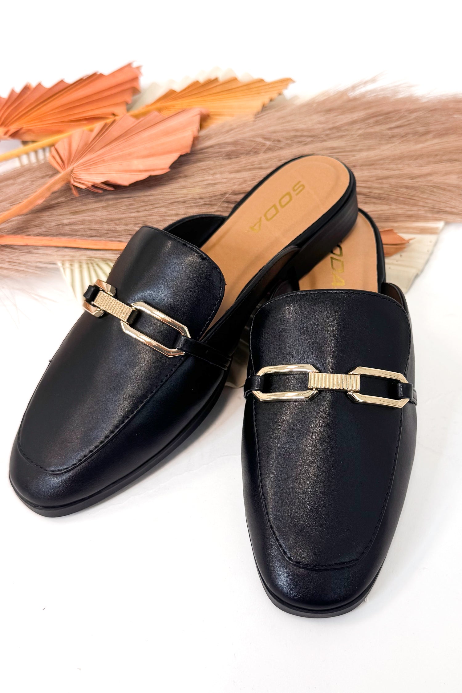 Black loafers with gold buckles on a white background