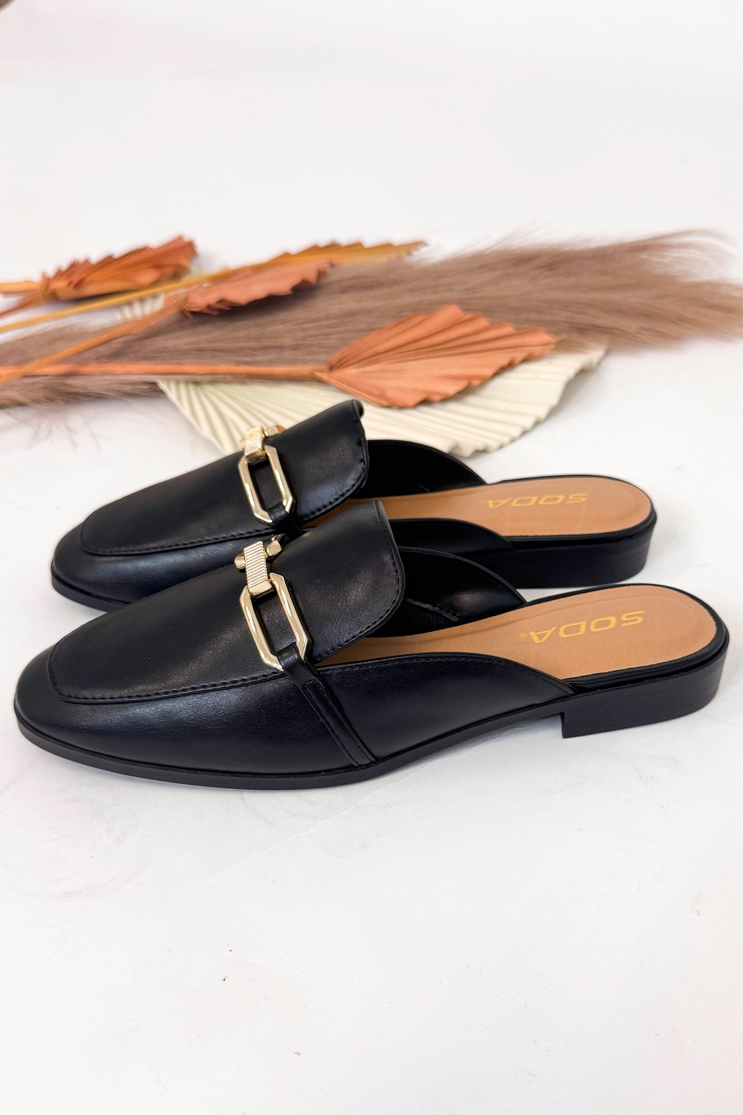 Black loafers with gold buckles on a white background