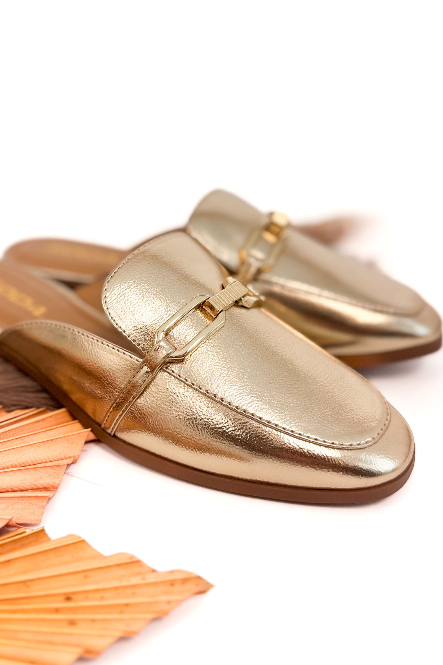 Gold loafers on a white background with wooden elements.