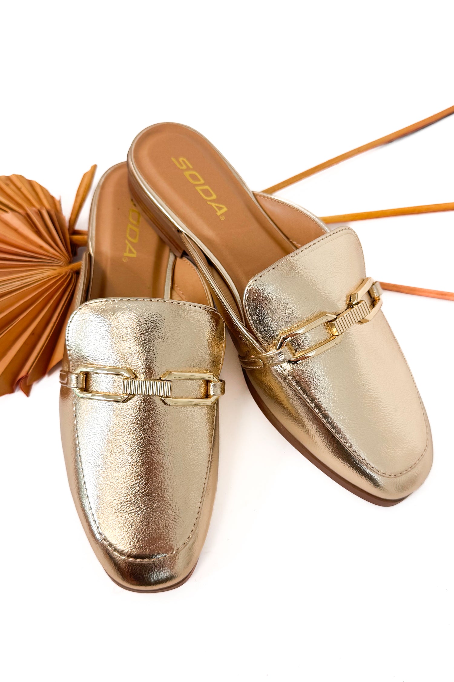 Gold metallic loafers with a decorative strap on a white background