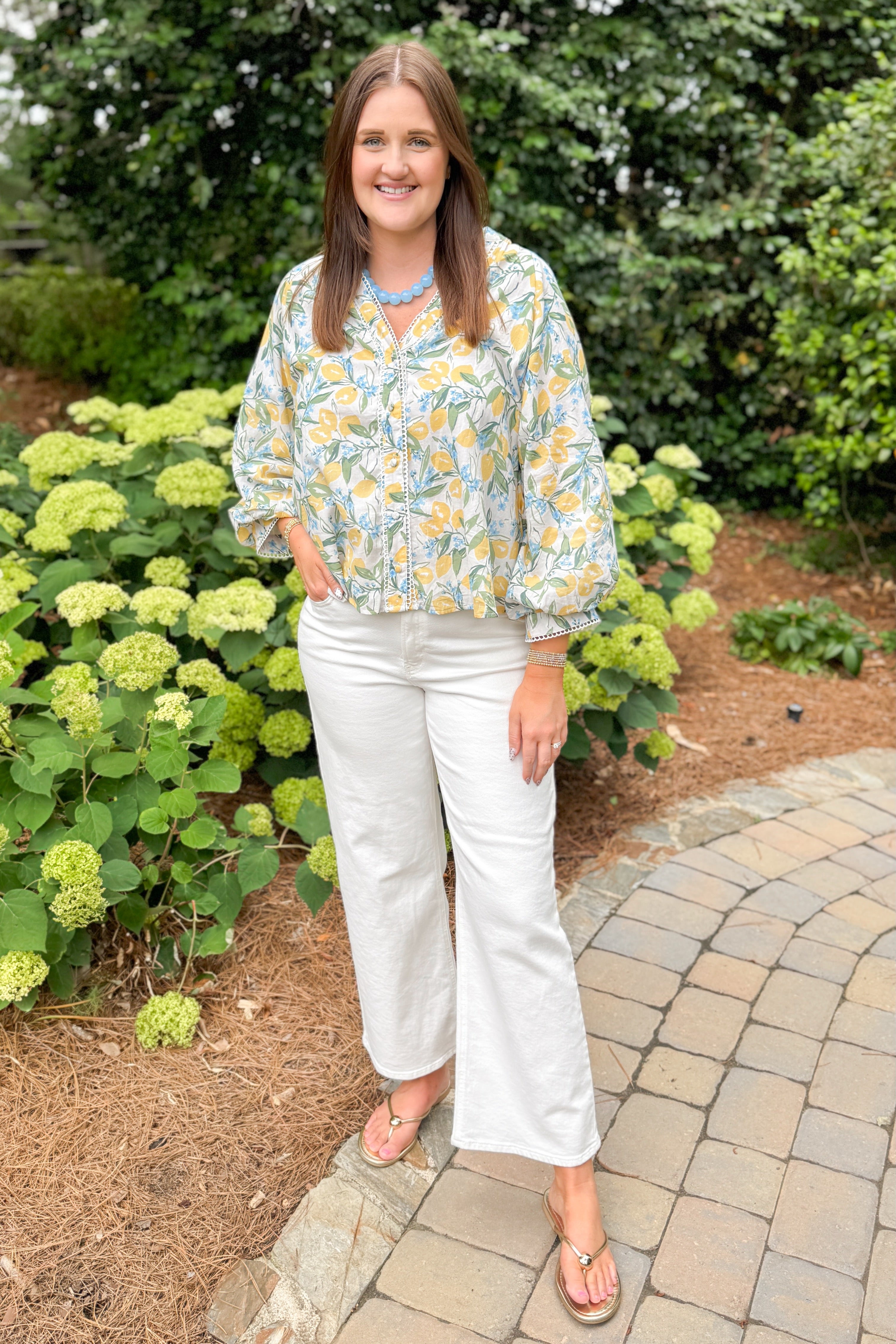 Front view of woman wearing Swagger Boutiqueās Yellow & Blue Lemon Print 3/4 Sleeve Top with jeans standing outside on a path.