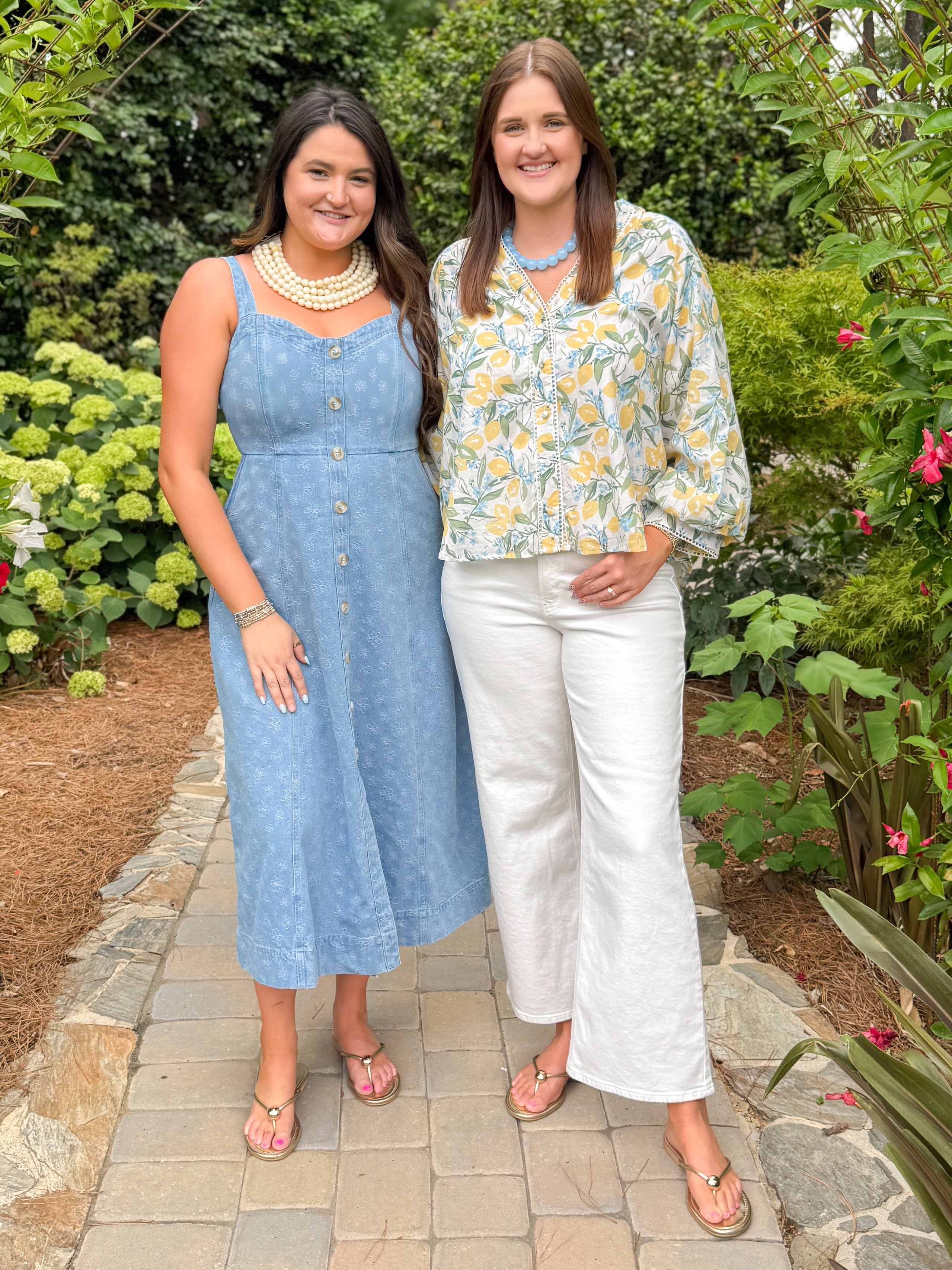 Front view of woman wearing Swagger Boutiqueās Yellow & Blue Lemon Print 3/4 Sleeve Top with jeans and woman wearing Blue floral print dress standing outside on a path.