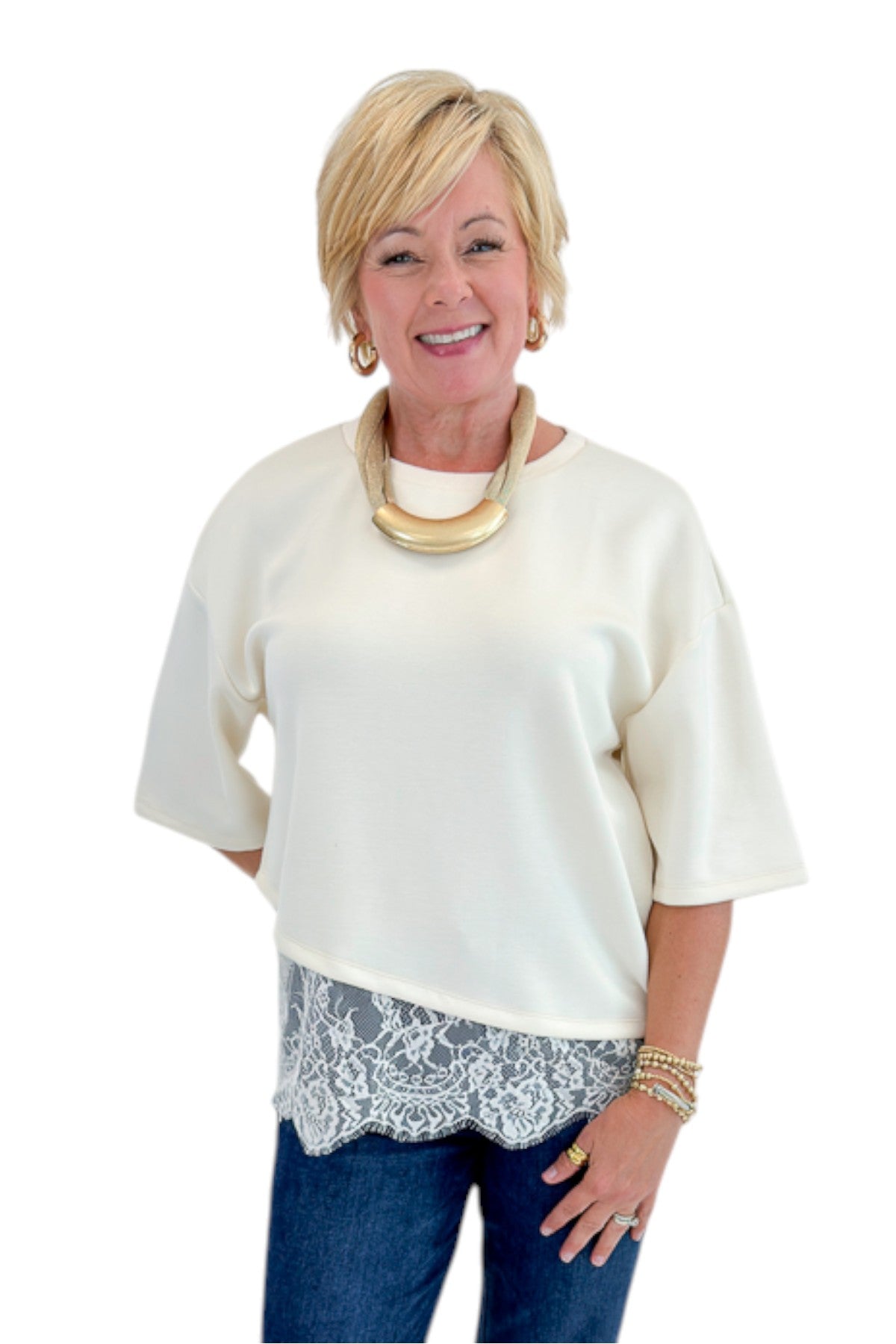Front view of woman wearing Swagger Boutique’s Ecru Asymmetrical Lace Hem Top by Entro with jeans against white studio background.
