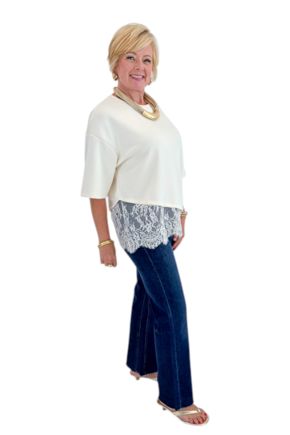 Side view of woman wearing Swagger Boutique’s Ecru Asymmetrical Lace Hem Top by Entro with jeans against white studio background.