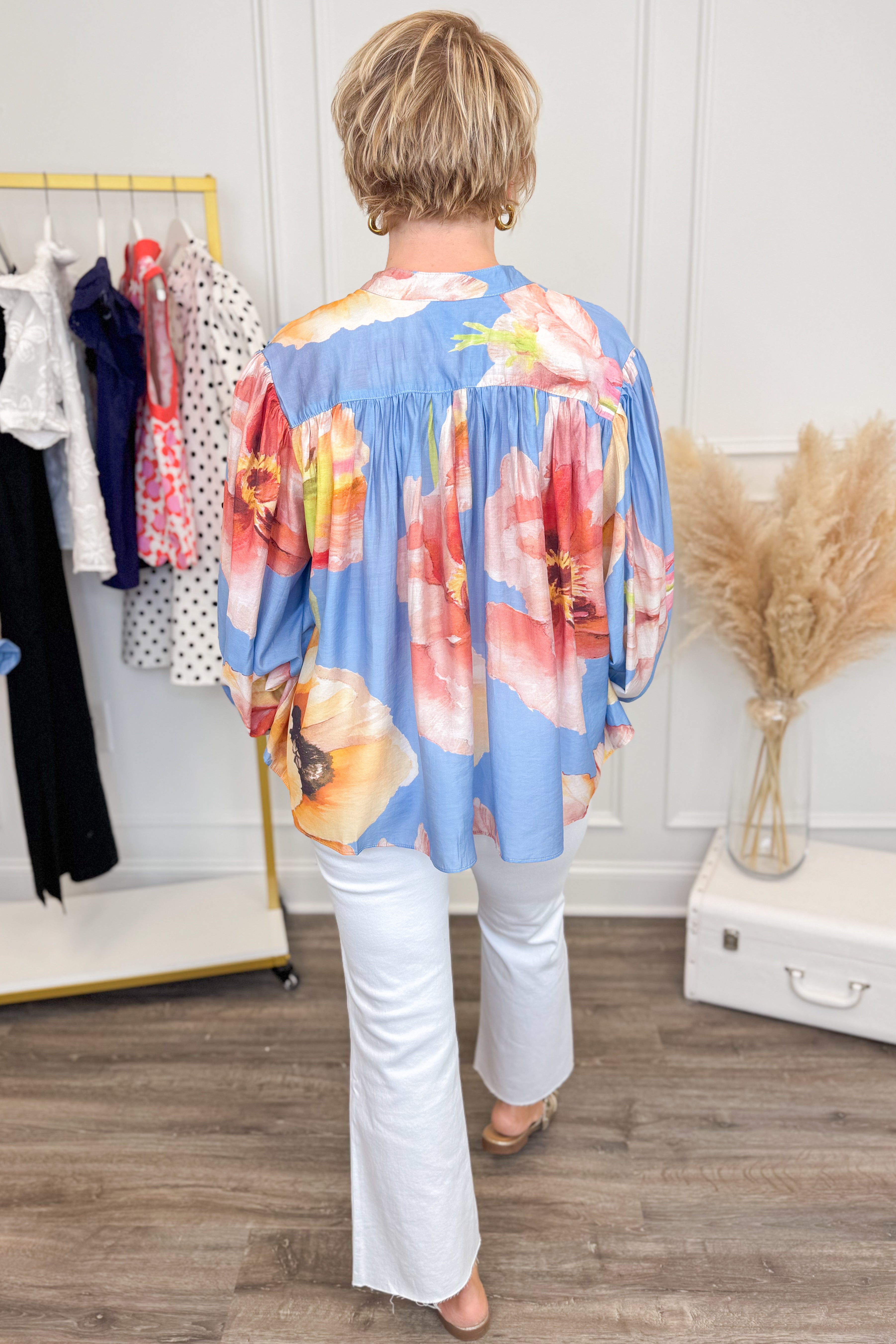 Person wearing a colorful floral top in a room with clothing racks and decor.