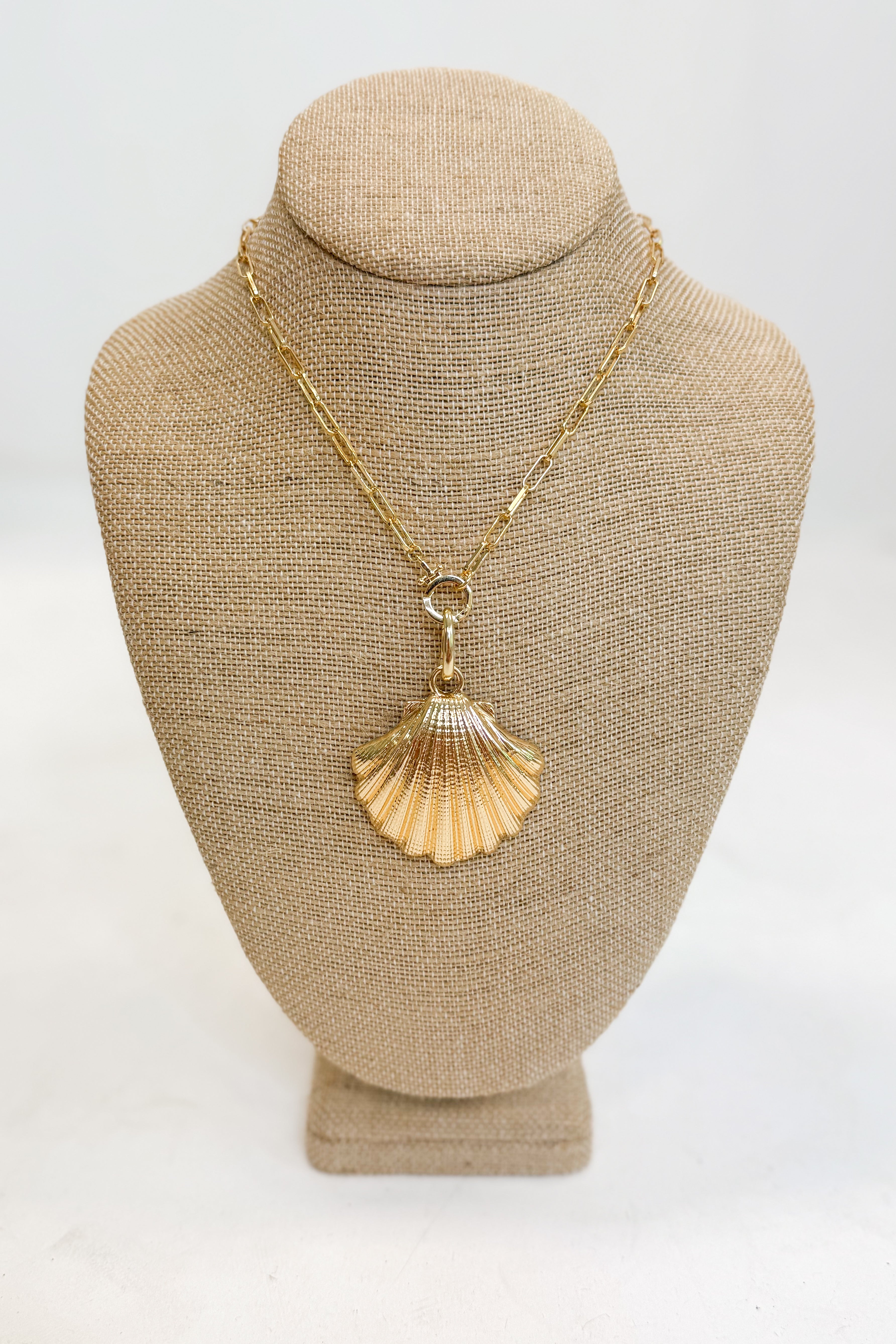 Gold necklace with a shell pendant on a beige mannequin bust against a white background