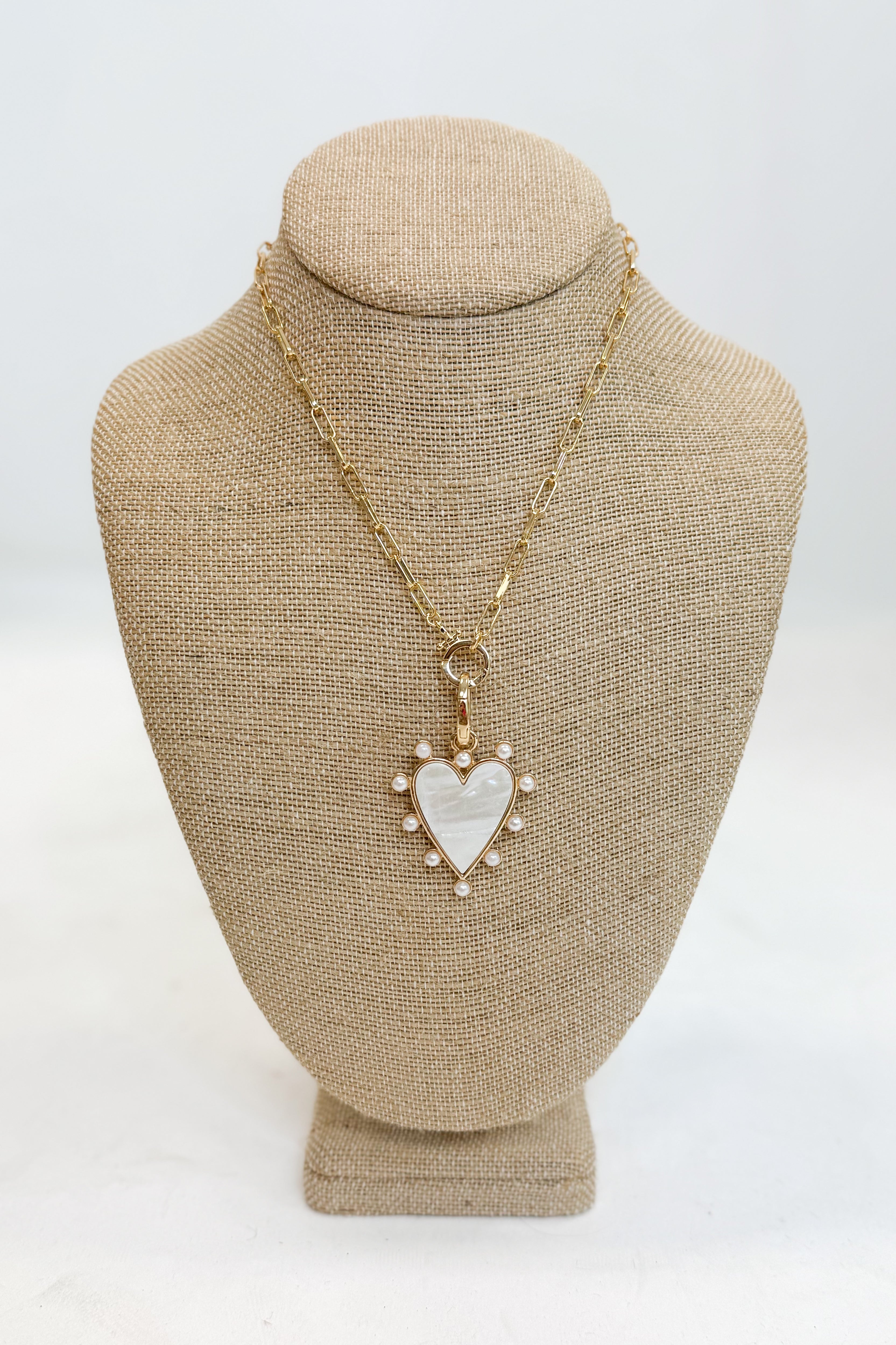 Gold necklace with a heart-shaped pendant on a beige bust against a white background